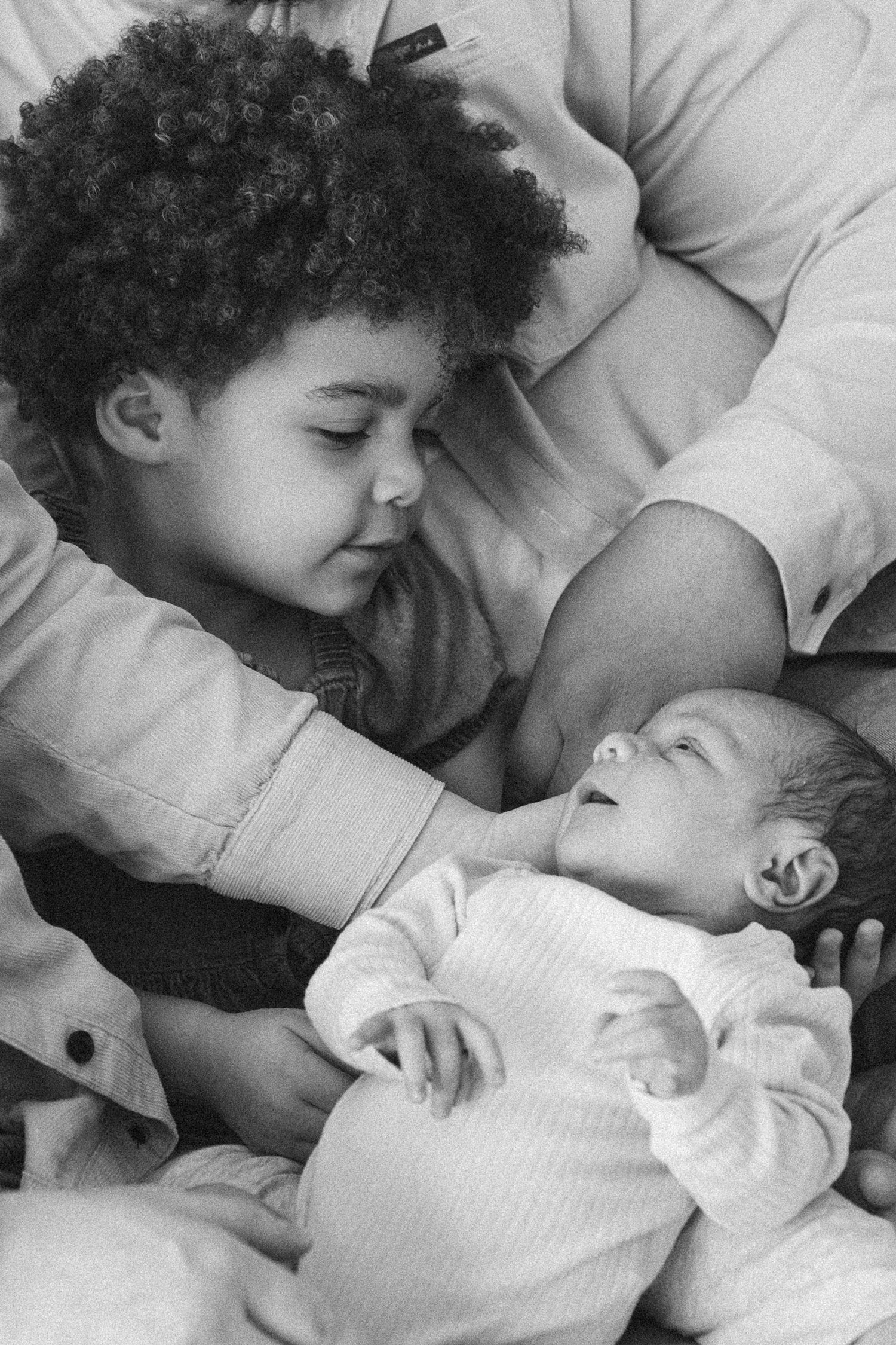 Black and white photo of a young curly-haired child gazing lovingly at a newborn baby.