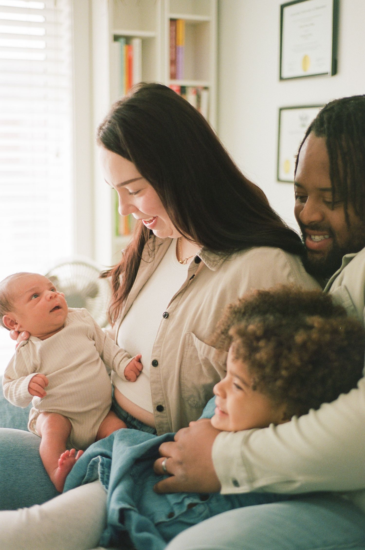 Happy interracial family smiling at newborn baby while sitting together on a couch at home.
