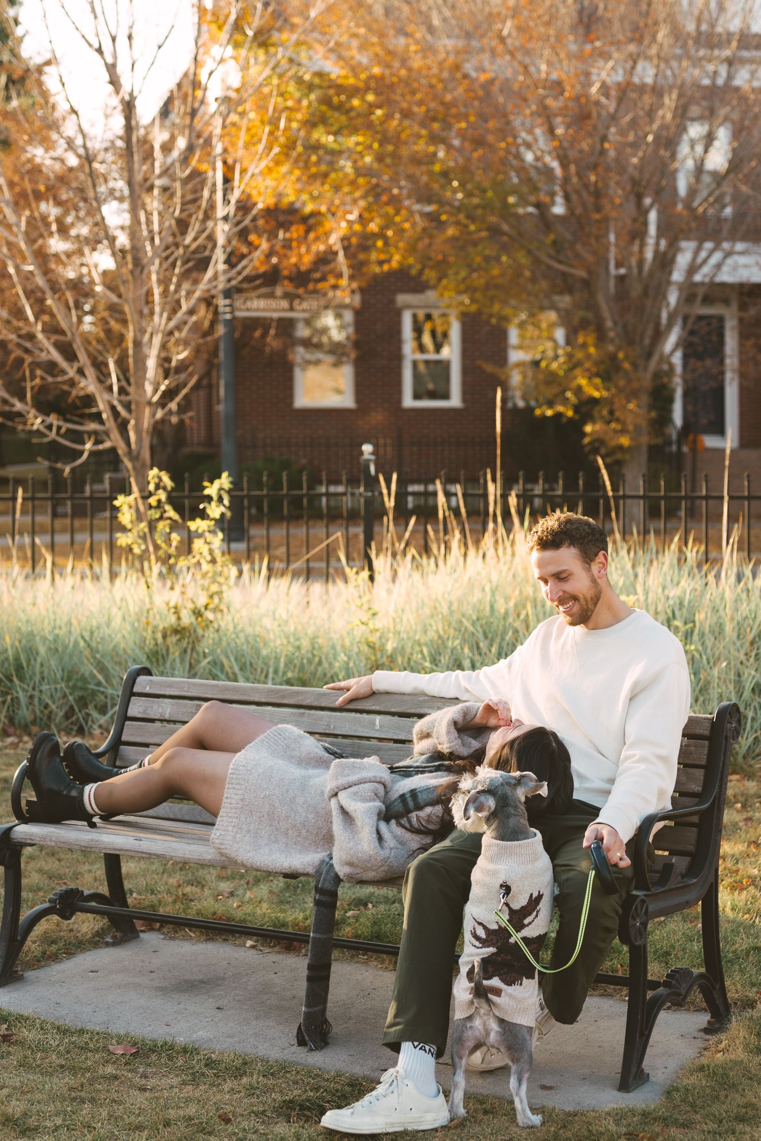 A person relaxes on a park bench with a small dog during a golden autumn afternoon.