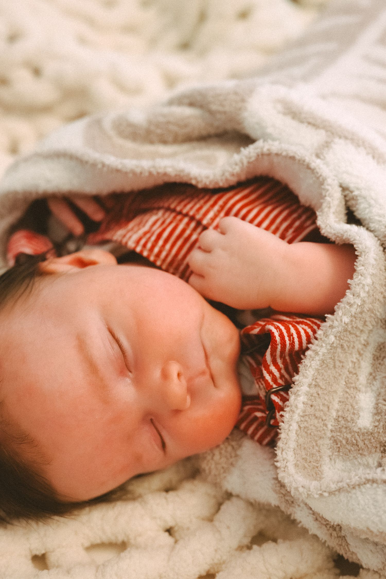 A peaceful sleeping infant wrapped in a white blanket wearing a red and white striped outfit.