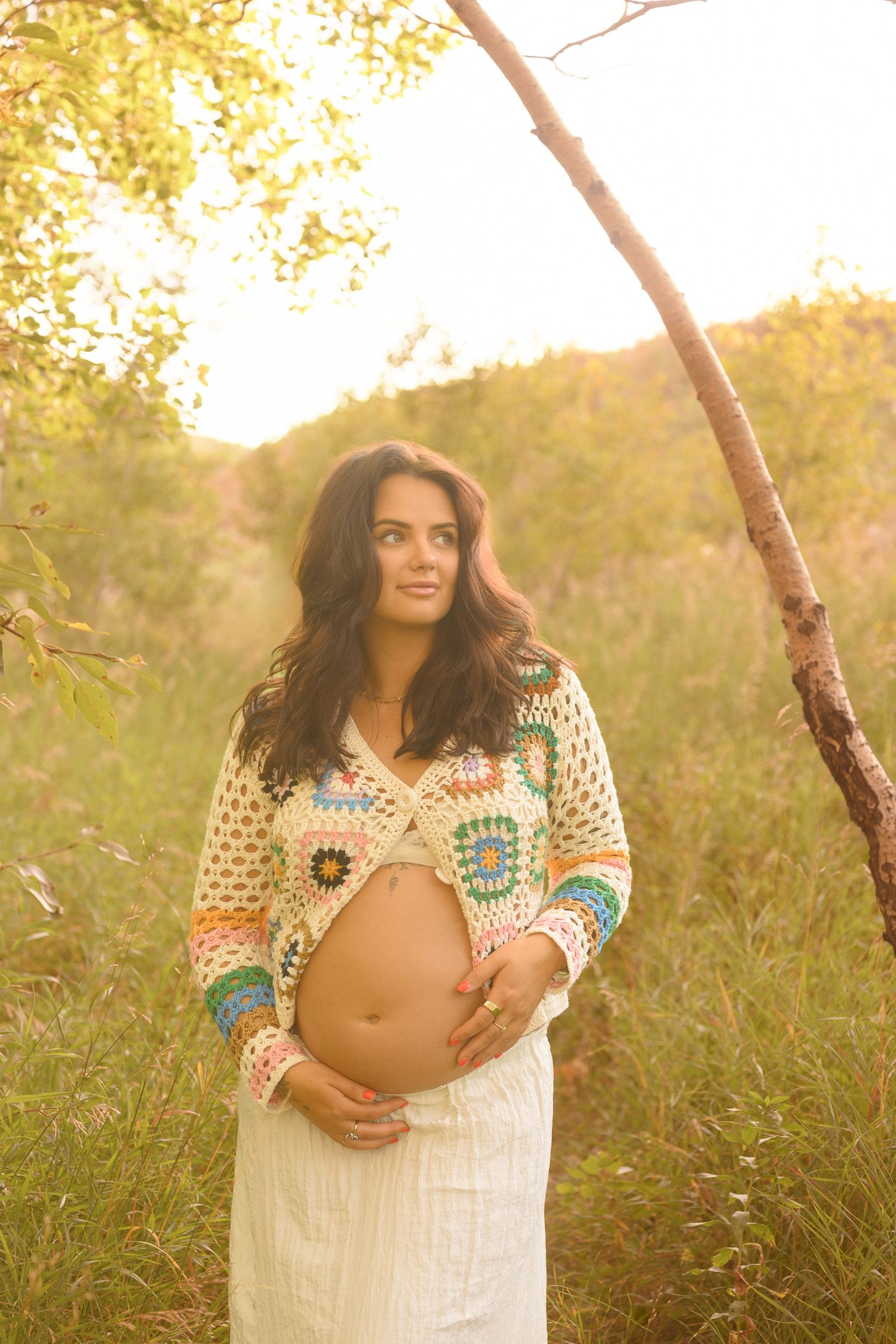Dreamy outdoor maternity photo with multicolored crochet sweater and white dress.