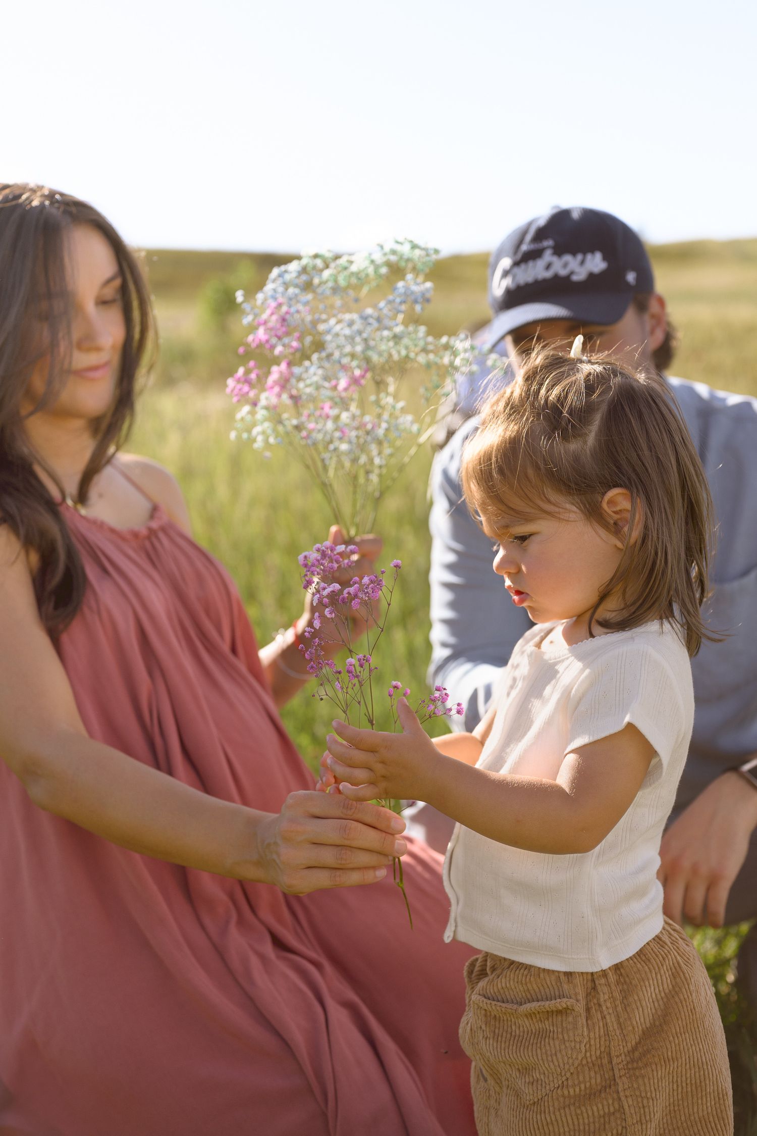 A small child holds delicate pink flowers while standing in a grassy meadow.