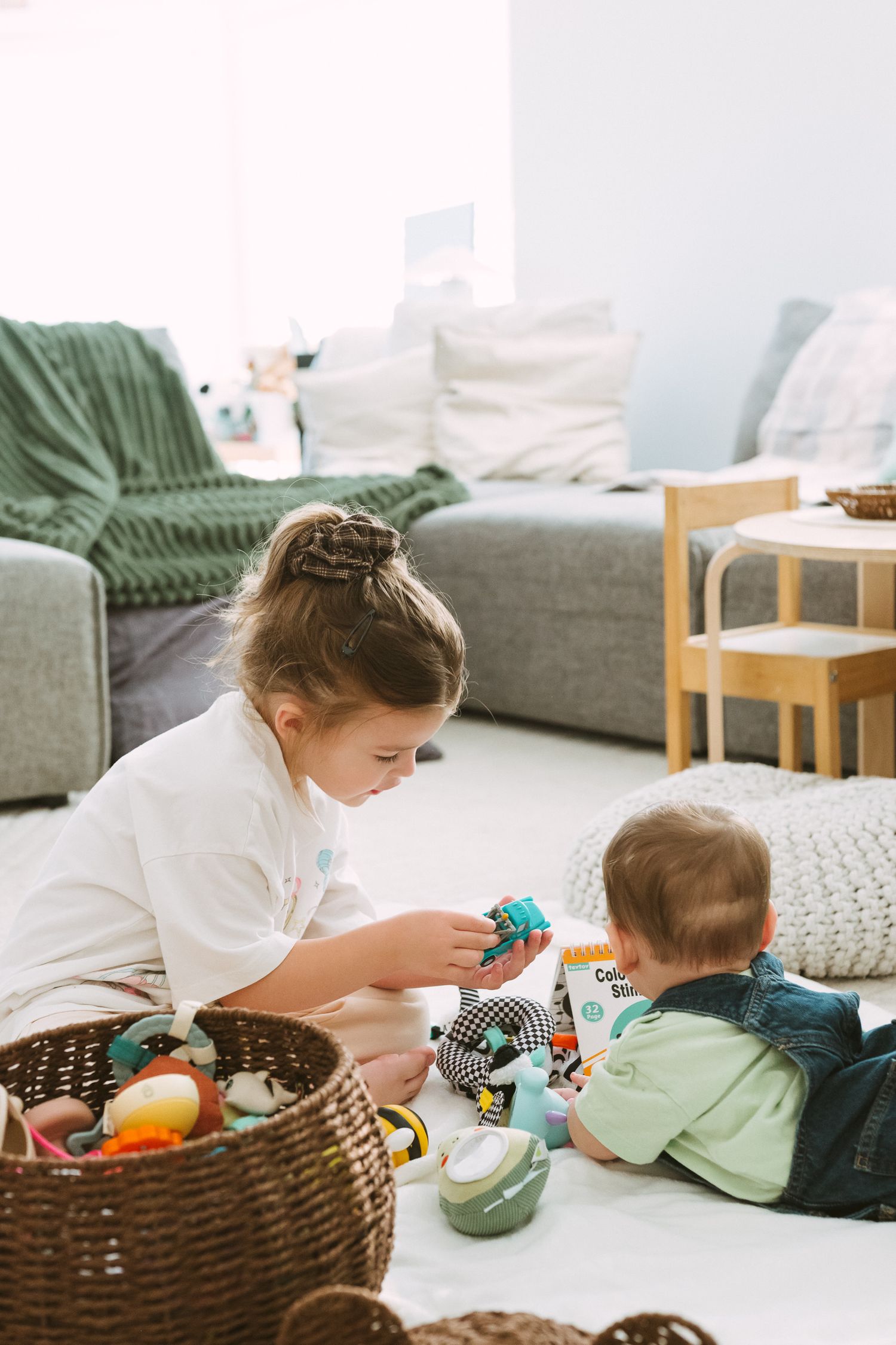 Children playing with colorful toys together on the floor near a brown woven basket.