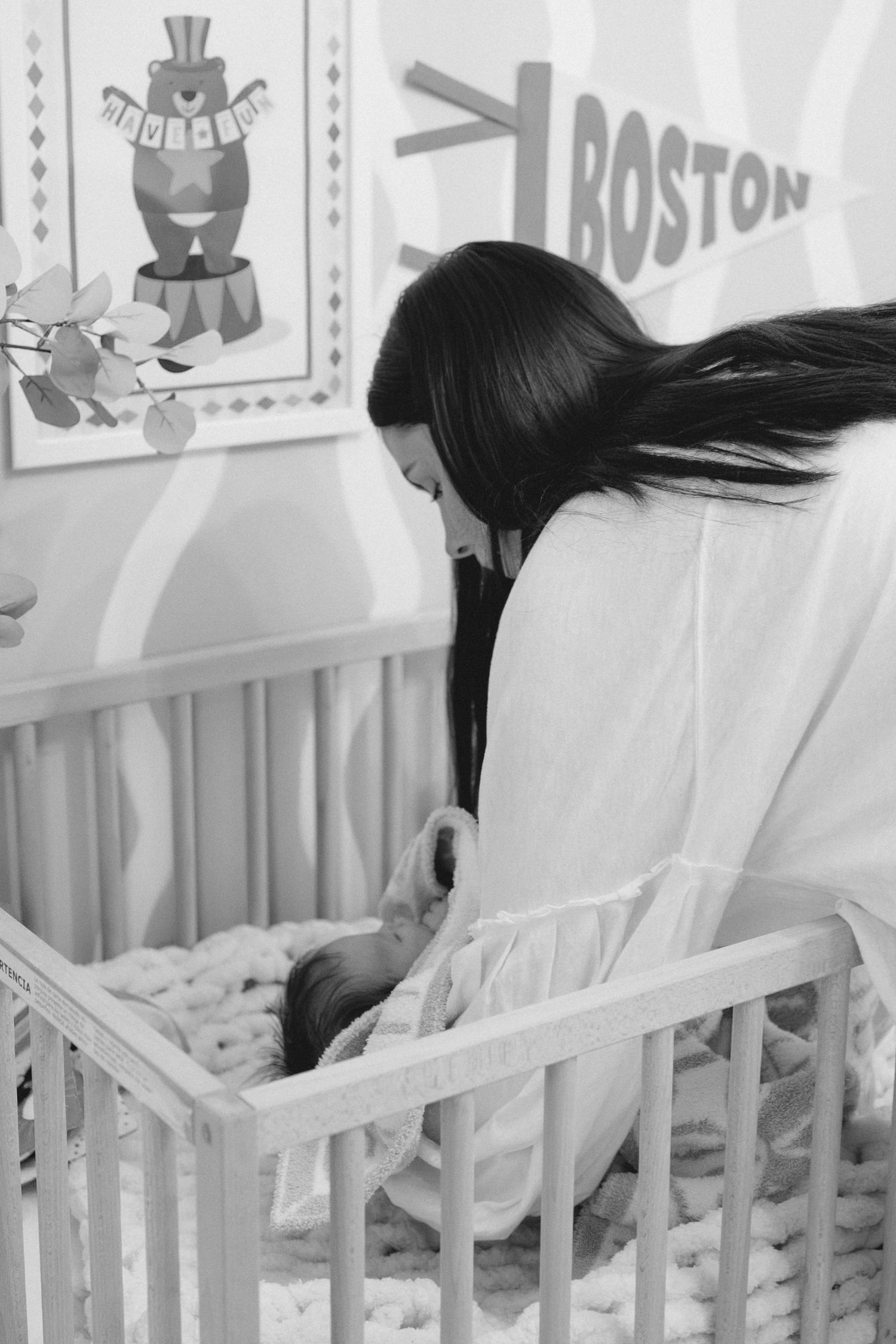 A person in white leans over a white crib in a nursery decorated with colorful wall art.