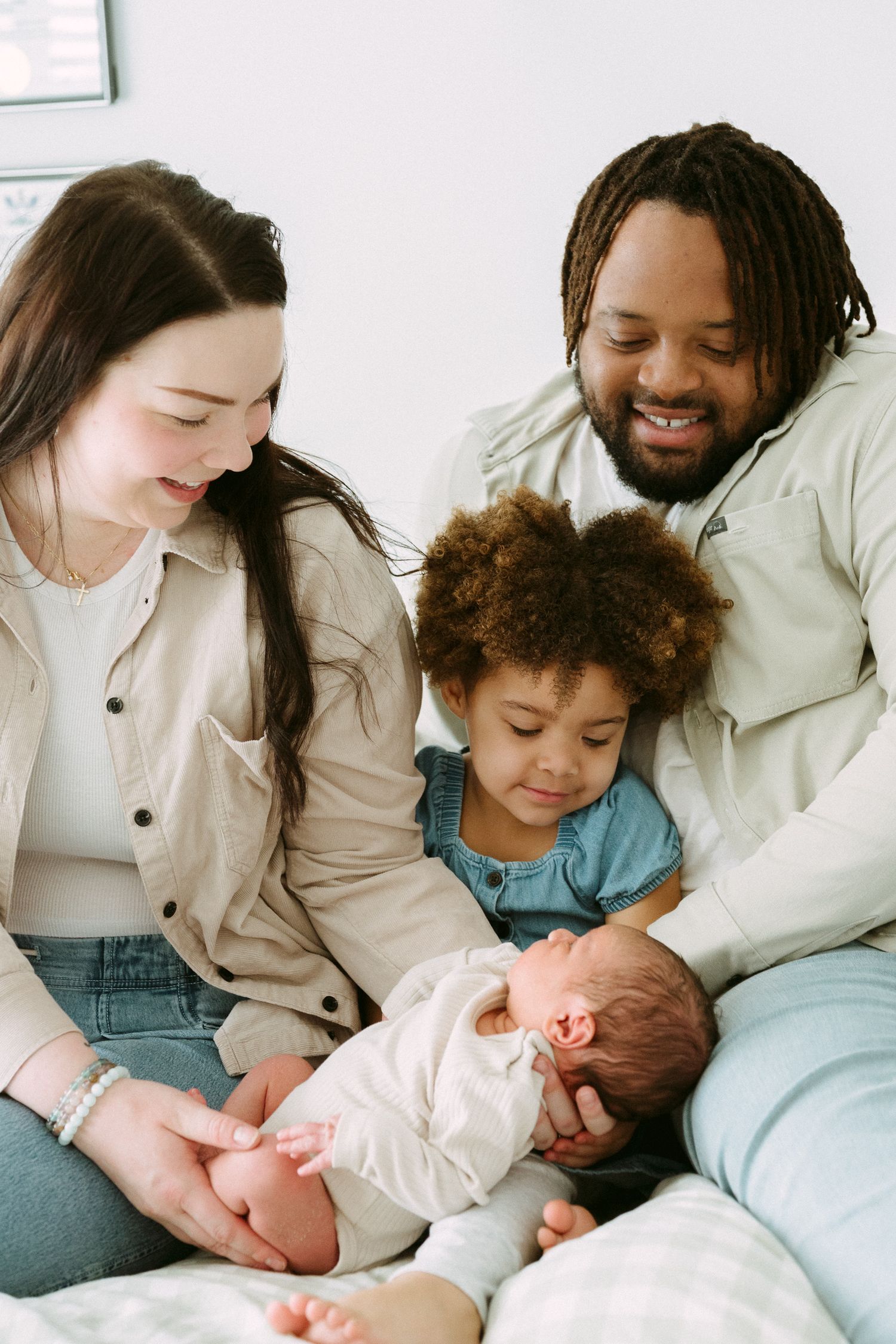 Happy interracial family with toddler and newborn baby bonding together on a couch at home.