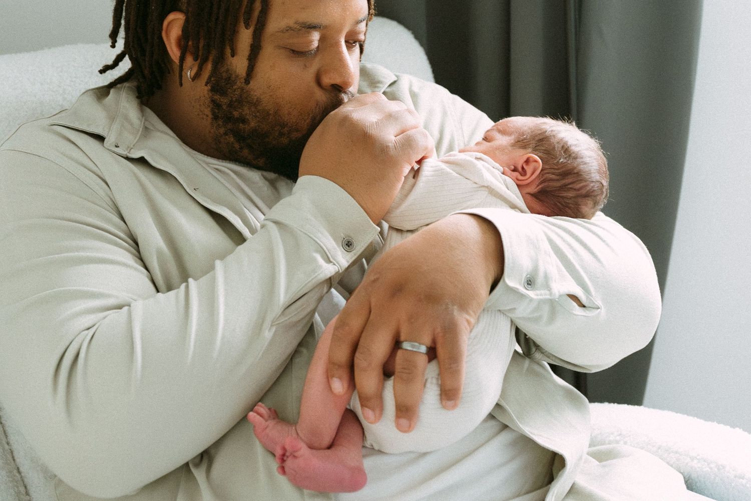 A father tenderly kisses his newborn baby while cradling the infant in his arms.