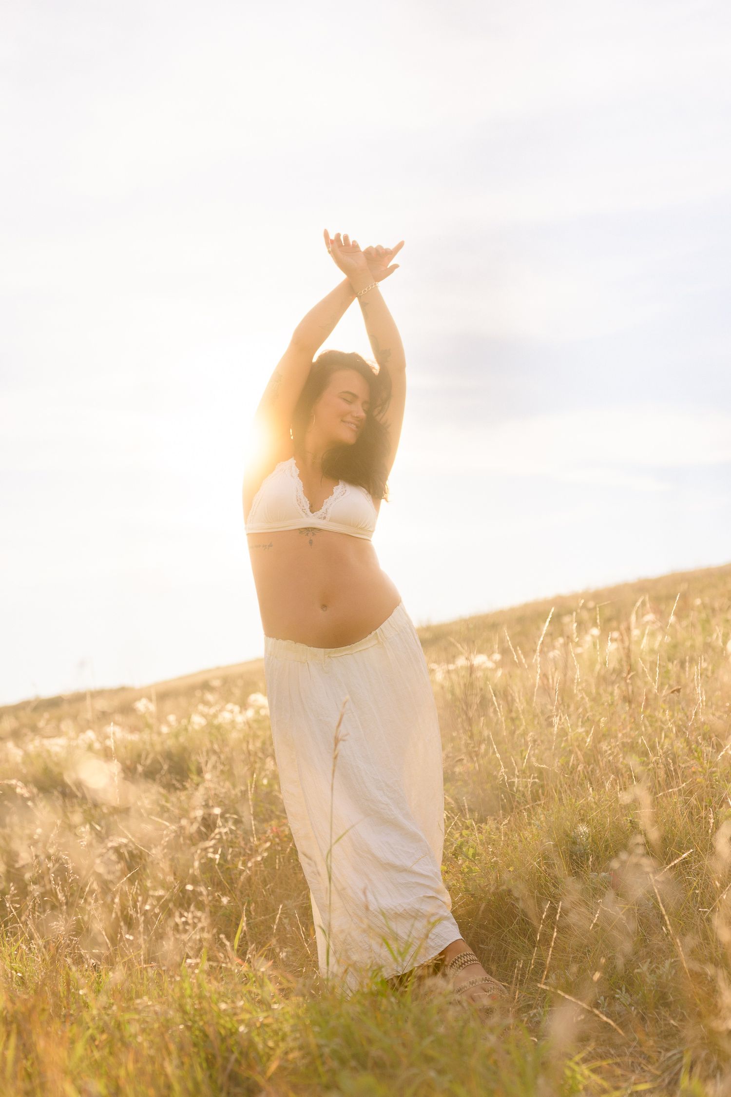 Joyful maternity dance poses captured in warm sunset light among tall grass.