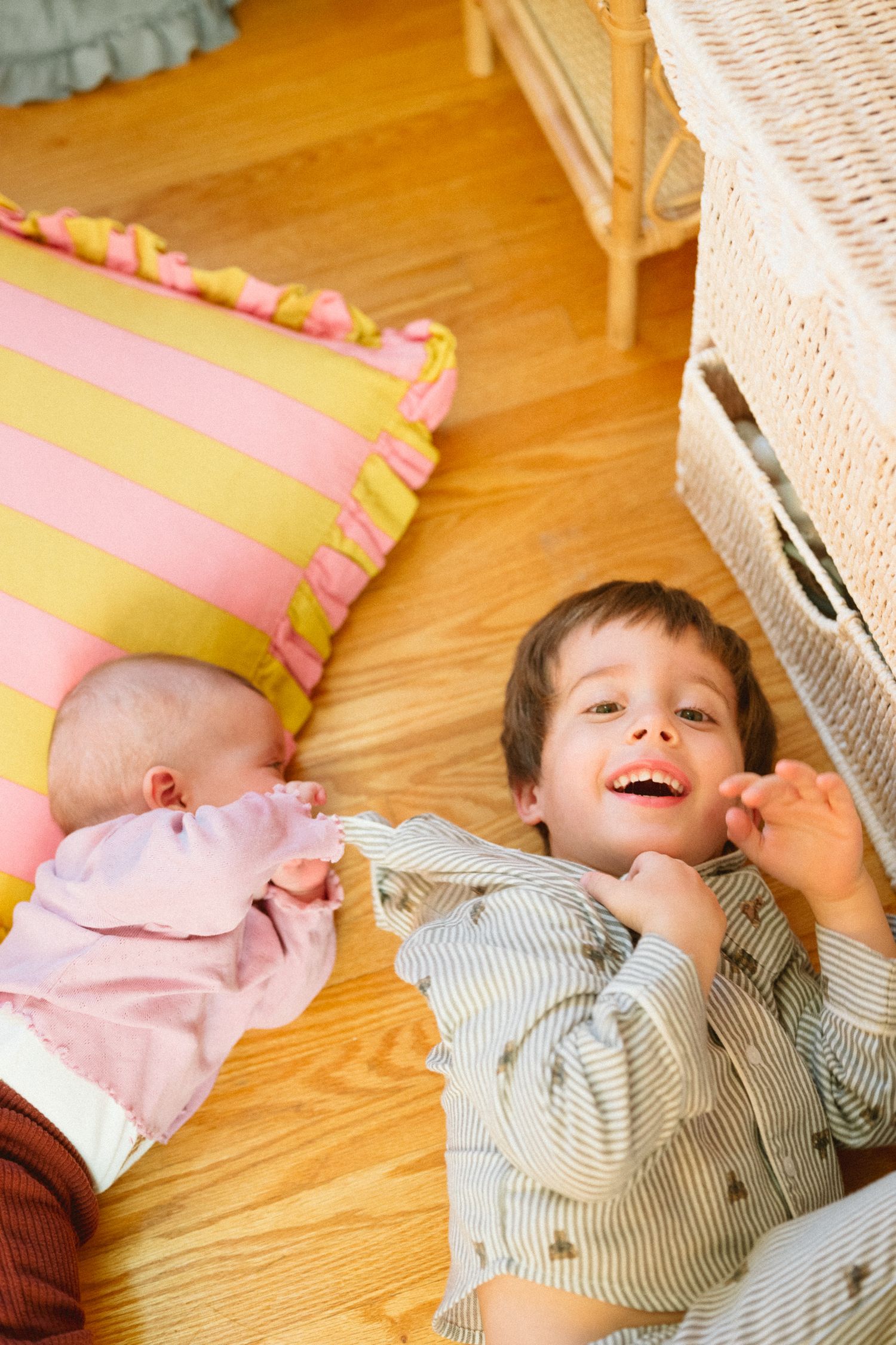 Children playing and laughing together on pink and yellow striped pillow near wicker furniture.