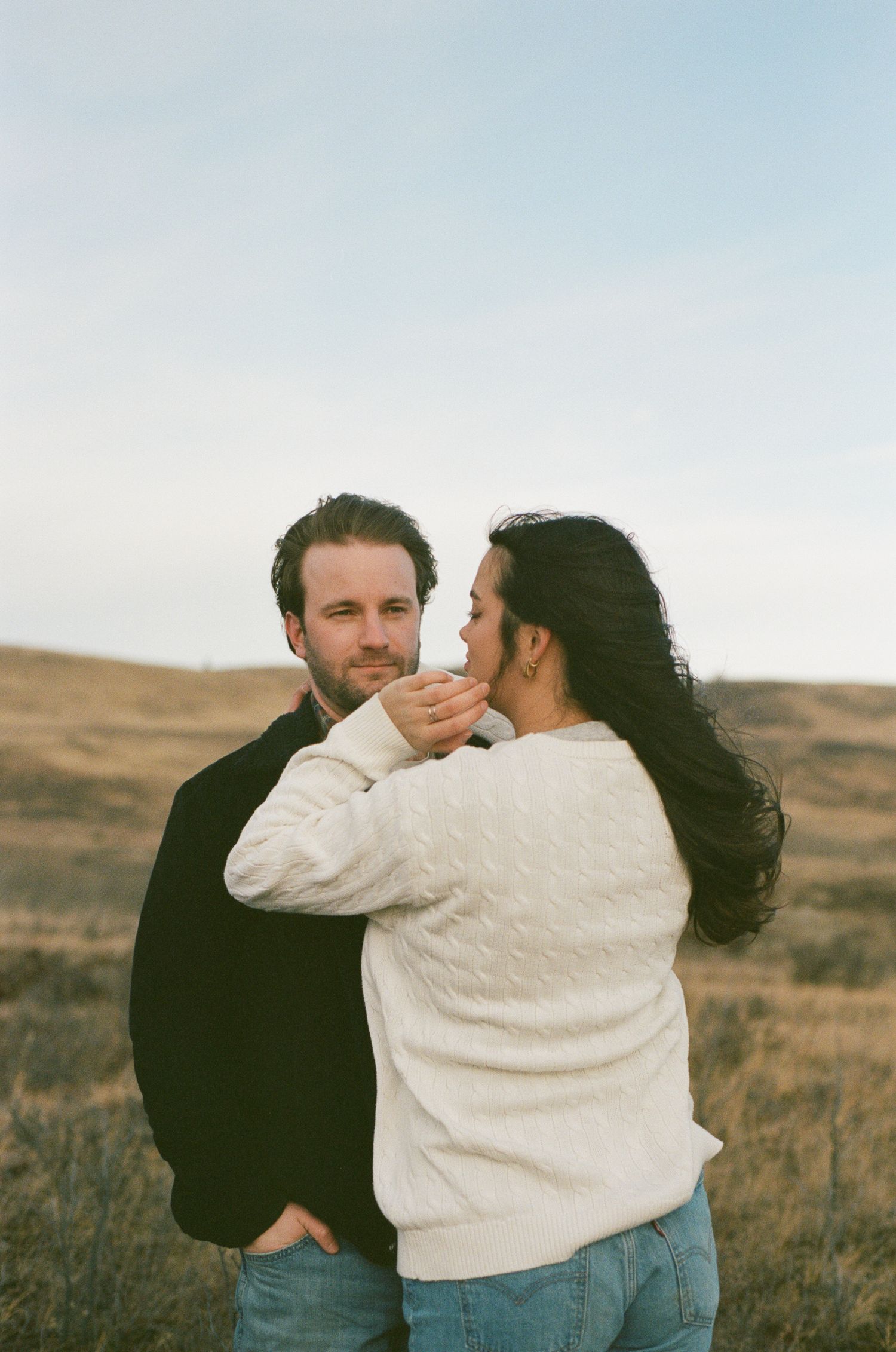 A tender moment between two people in white and black clothing against a rural landscape.