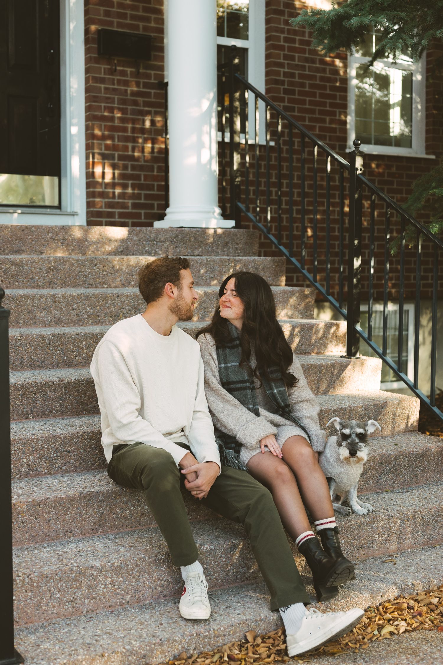 A couple sits together on brick building steps with their cat, sharing a romantic autumn moment.