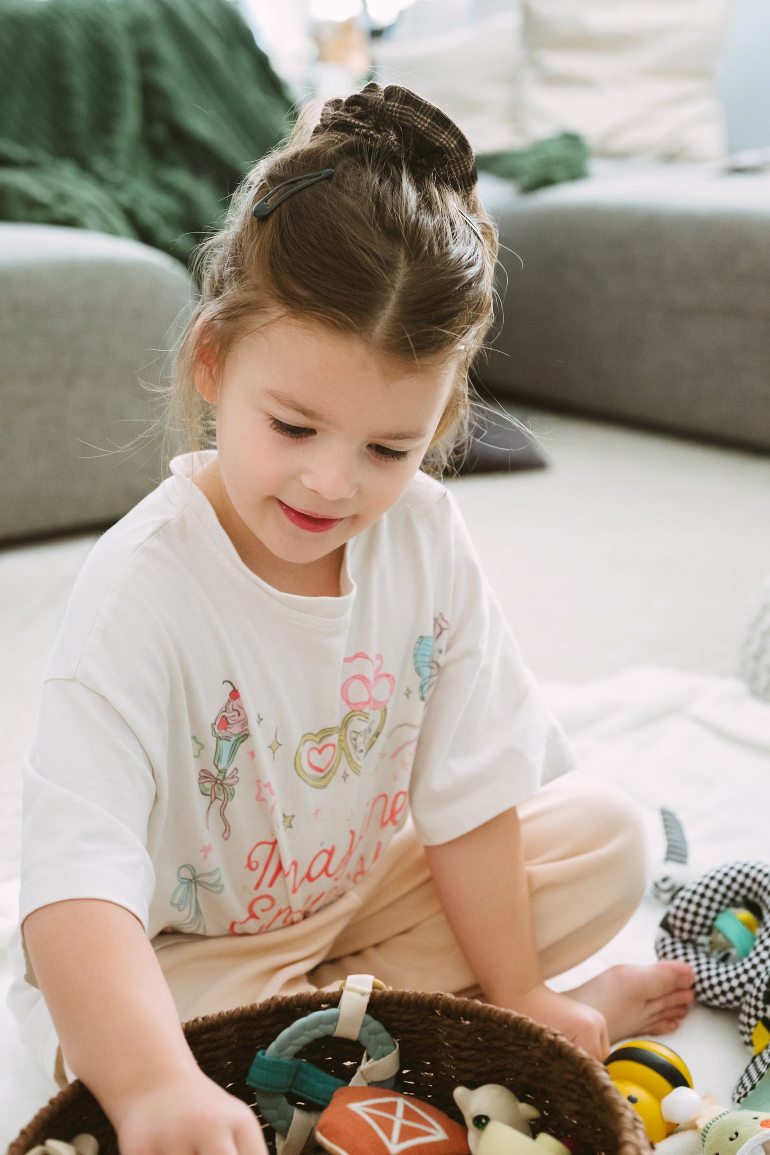 Young child in white t-shirt playing with toys while sitting on floor.