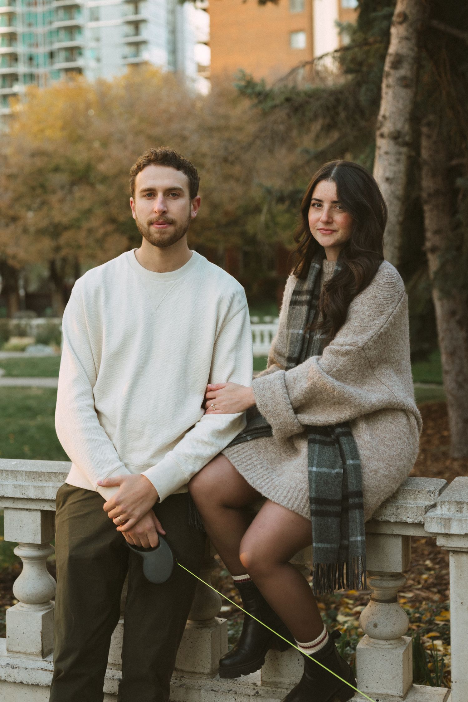 Two people in casual attire share a moment on stone steps surrounded by fall foliage.