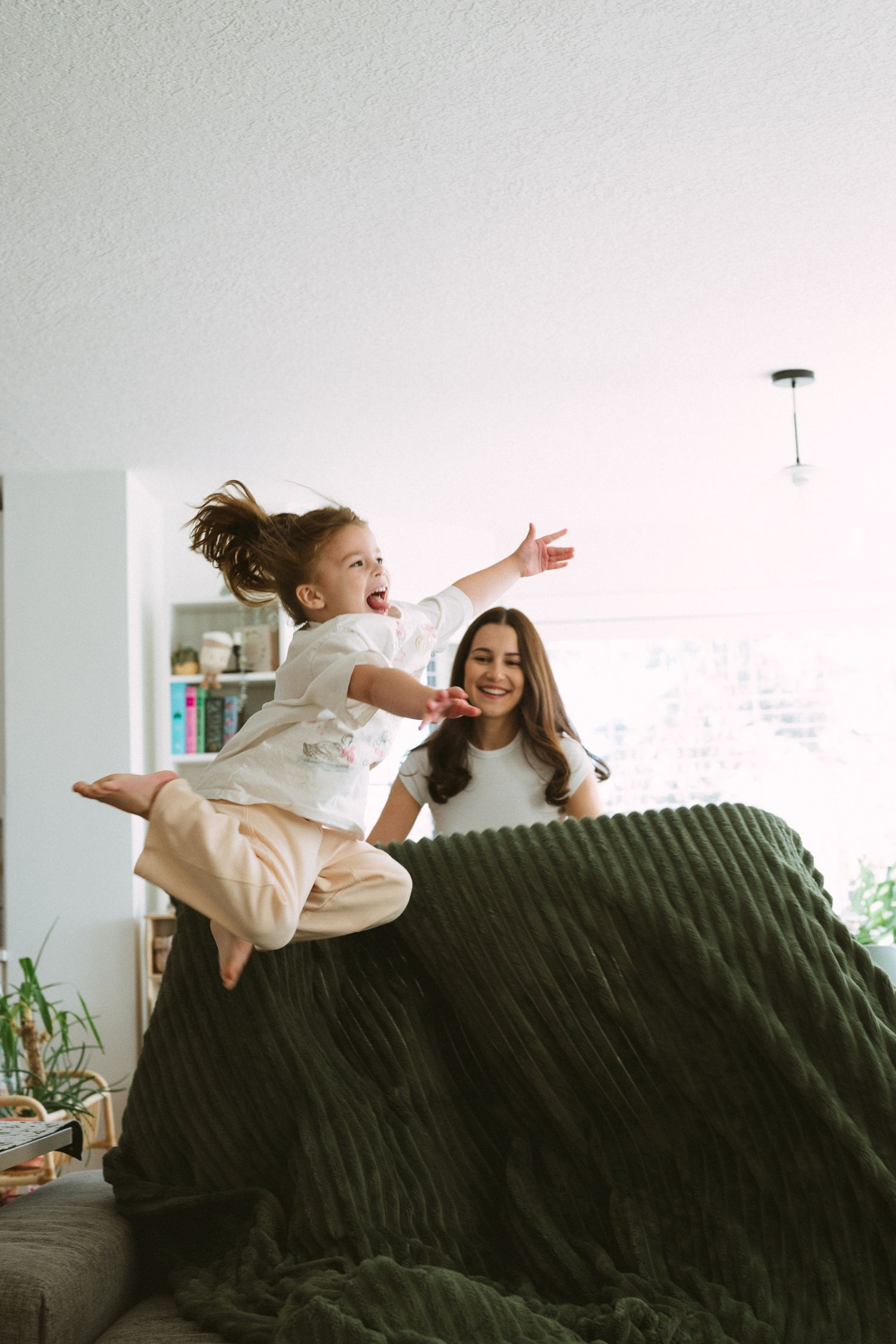 A couple playfully lounges and stretches on a dark couch in a bright, modern living room setting.