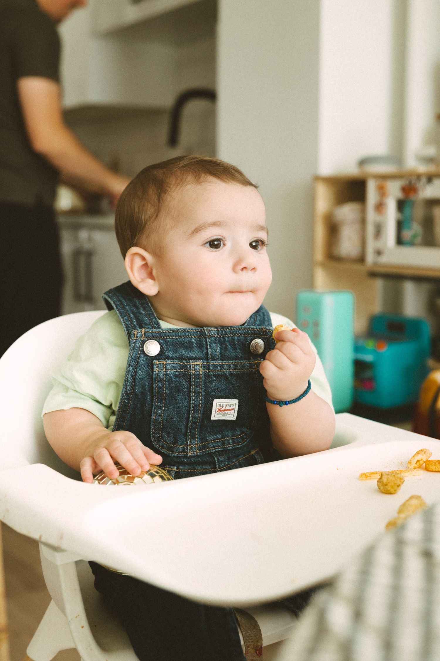 A baby in denim overalls sits in a white high chair during mealtime, shown from multiple angles.