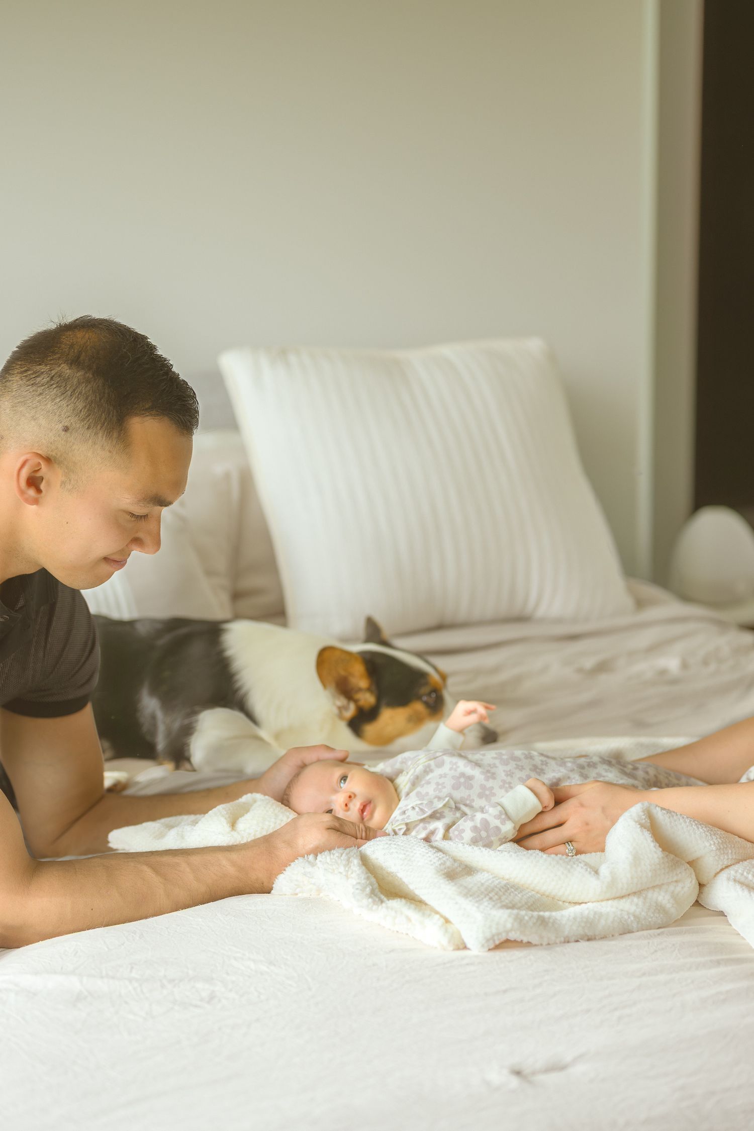 Tender moment captured between adult and sleeping infant on white bed.