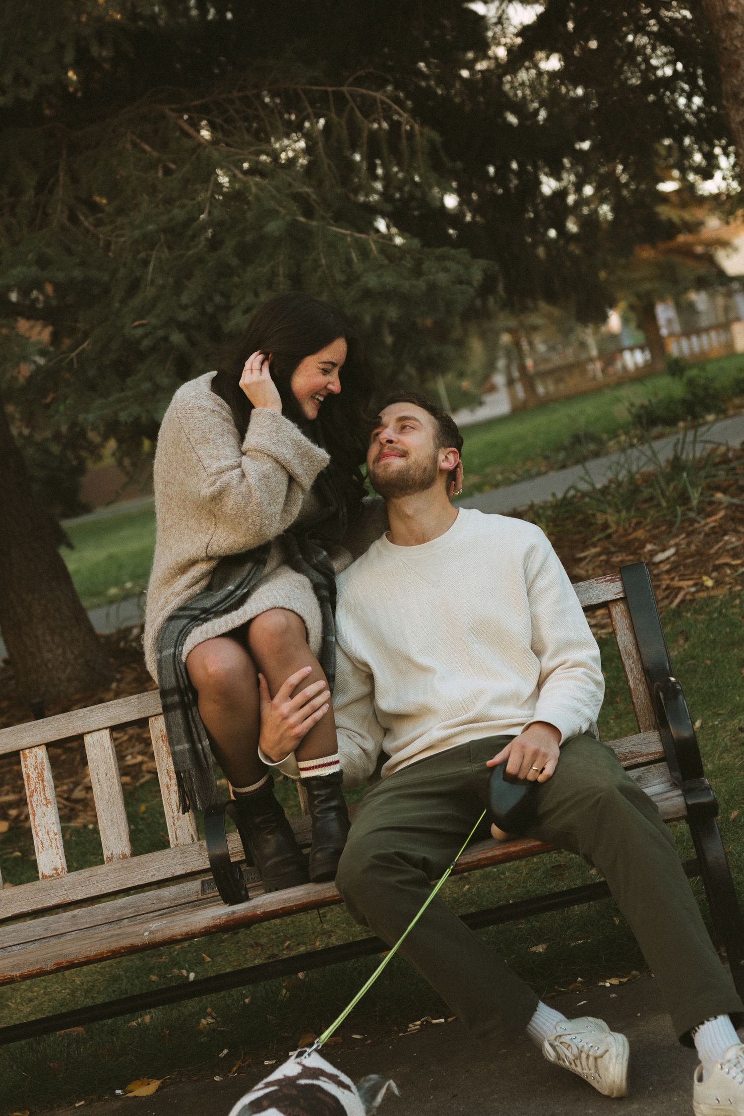 A couple sharing a joyful moment together while sitting on a wooden park bench in autumn.