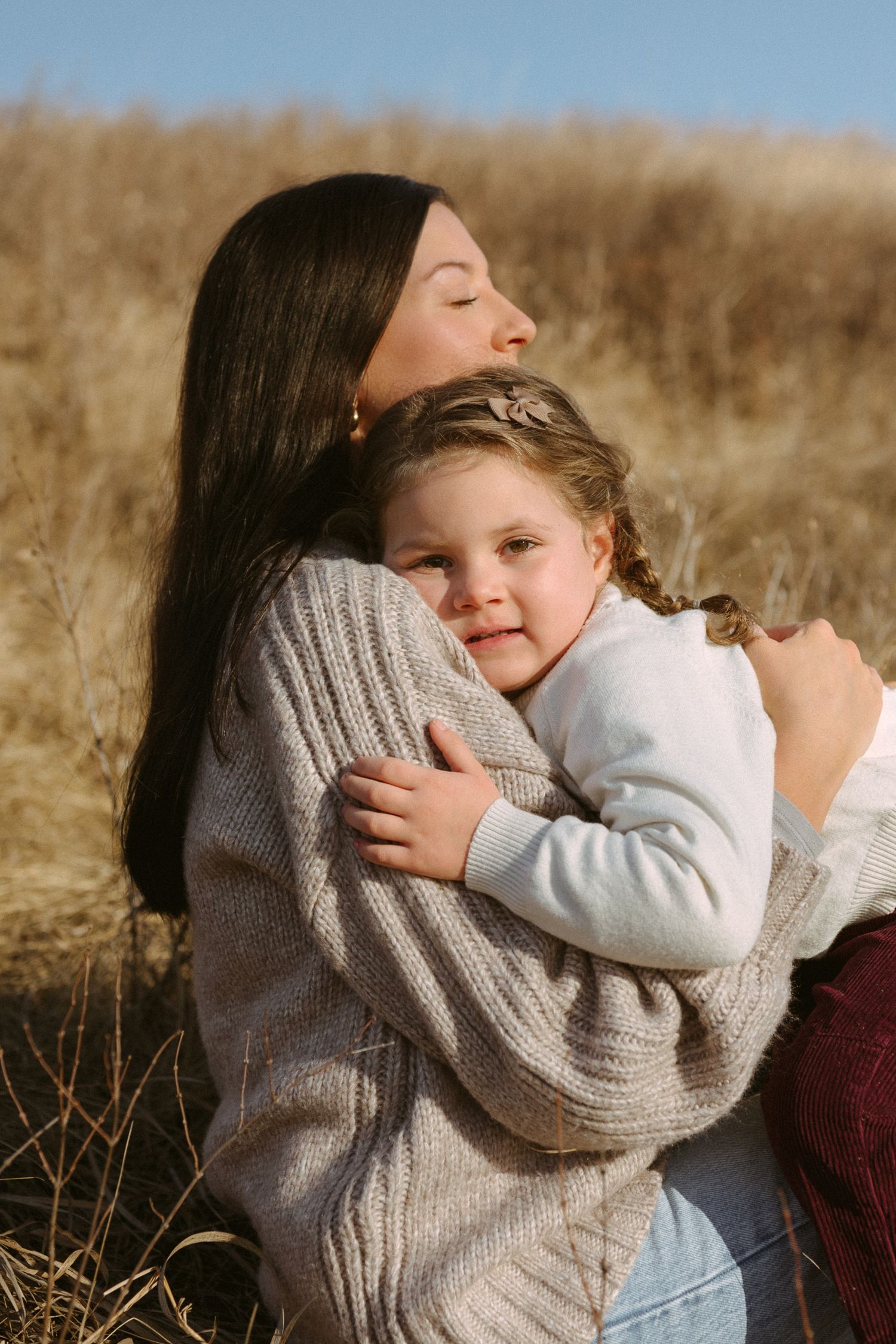 A tender embrace shared between two people sitting in tall dry grass on a sunny afternoon.