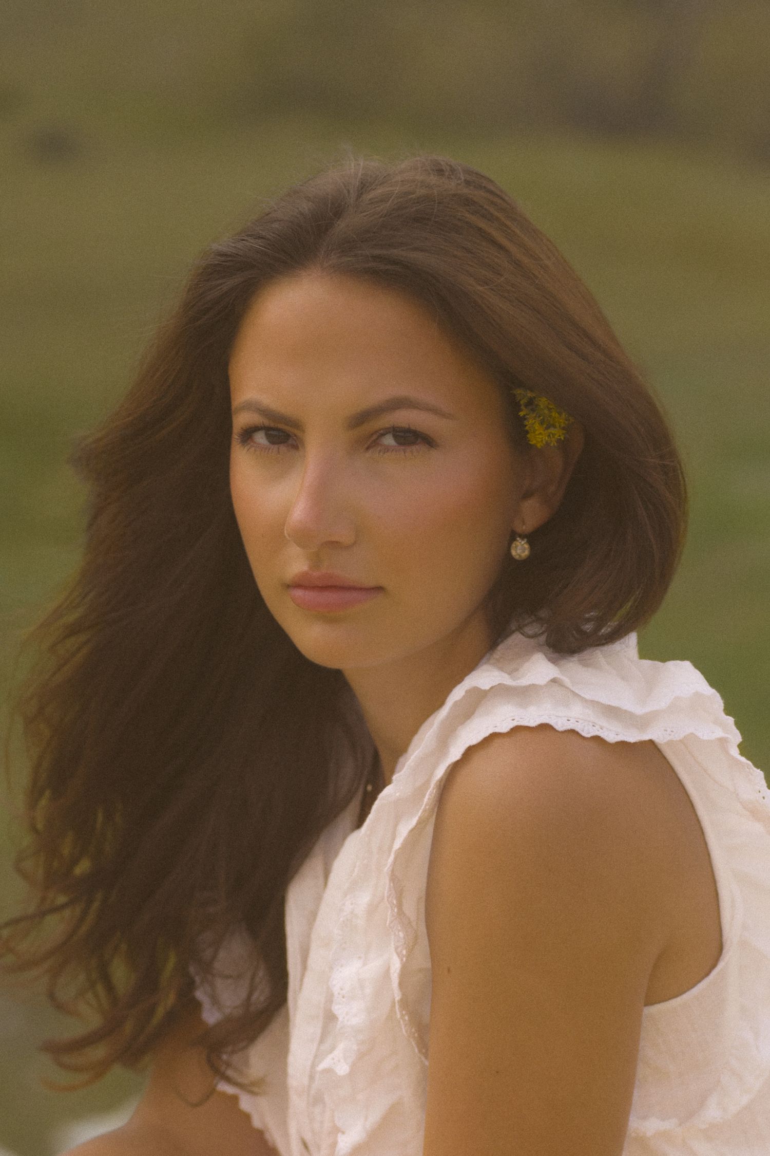 Artistic portrait with a small yellow flower accent against a natural summer backdrop.