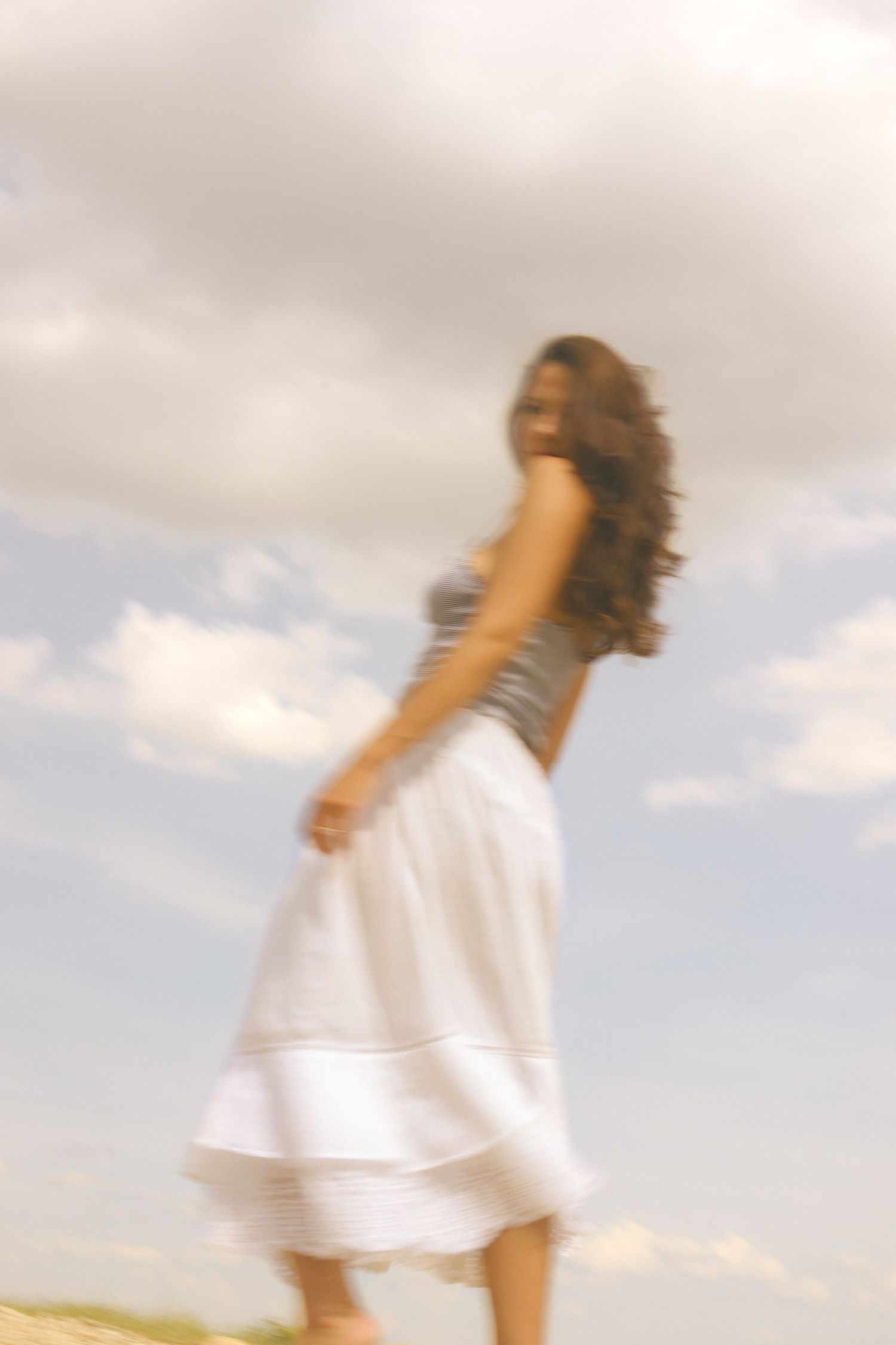 Someone in a white skirt and gray top dances in a field on a cloudy day.