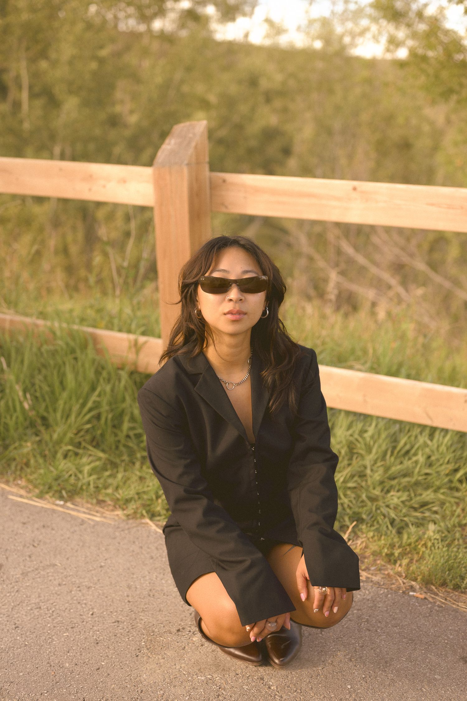 A person in sunglasses and black clothing poses near a wooden fence at sunset.