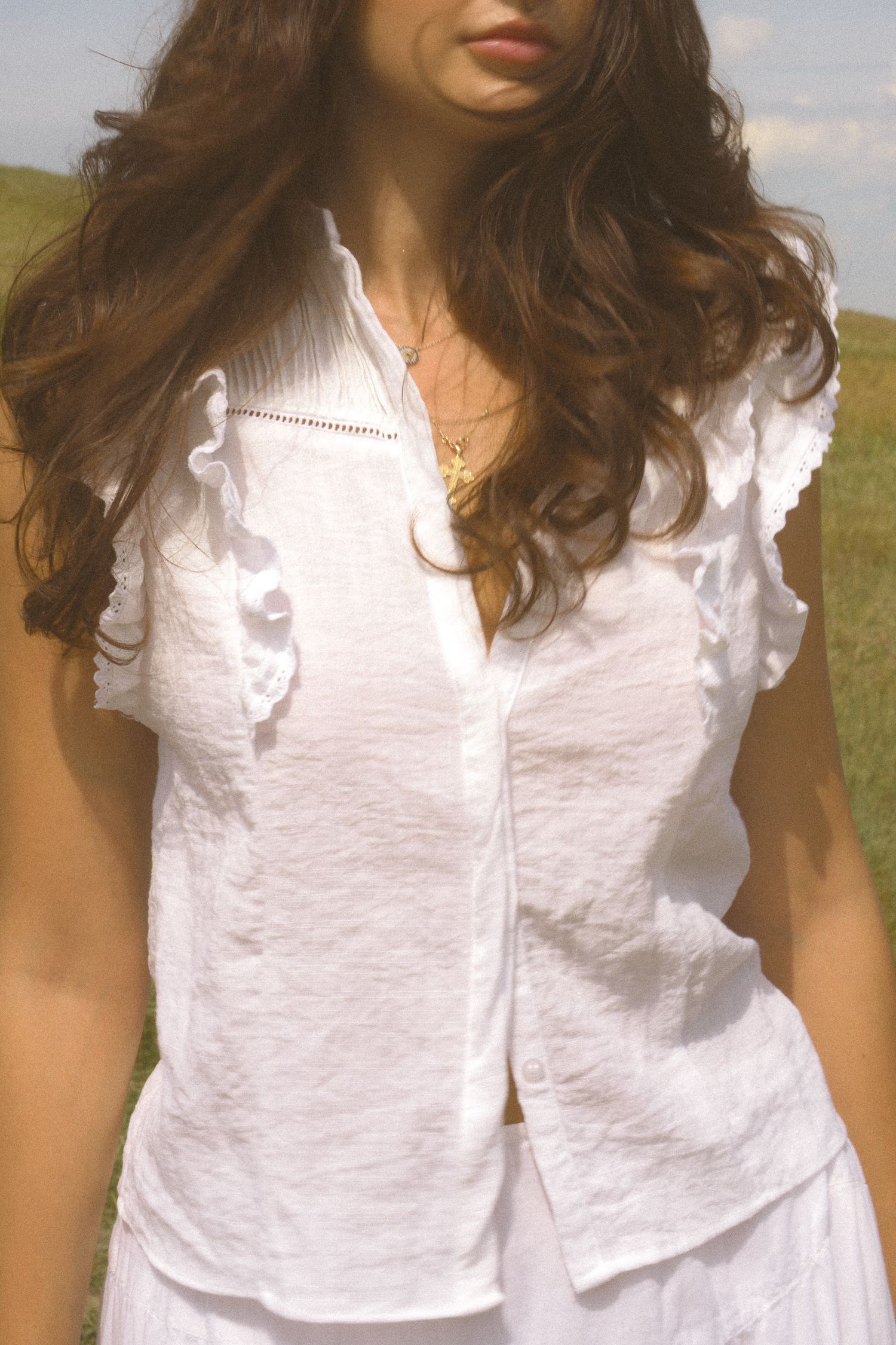 Detailed view of a white ruffled sleeveless top with textured fabric in natural lighting.