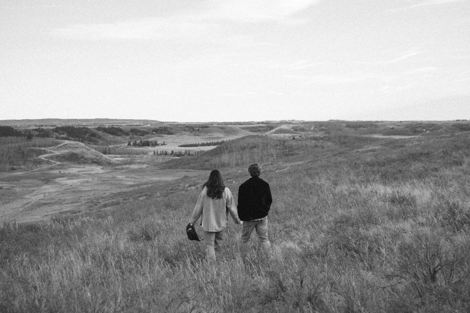 Black and white landscape photograph of rolling hills with people walking through tall prairie grass.
