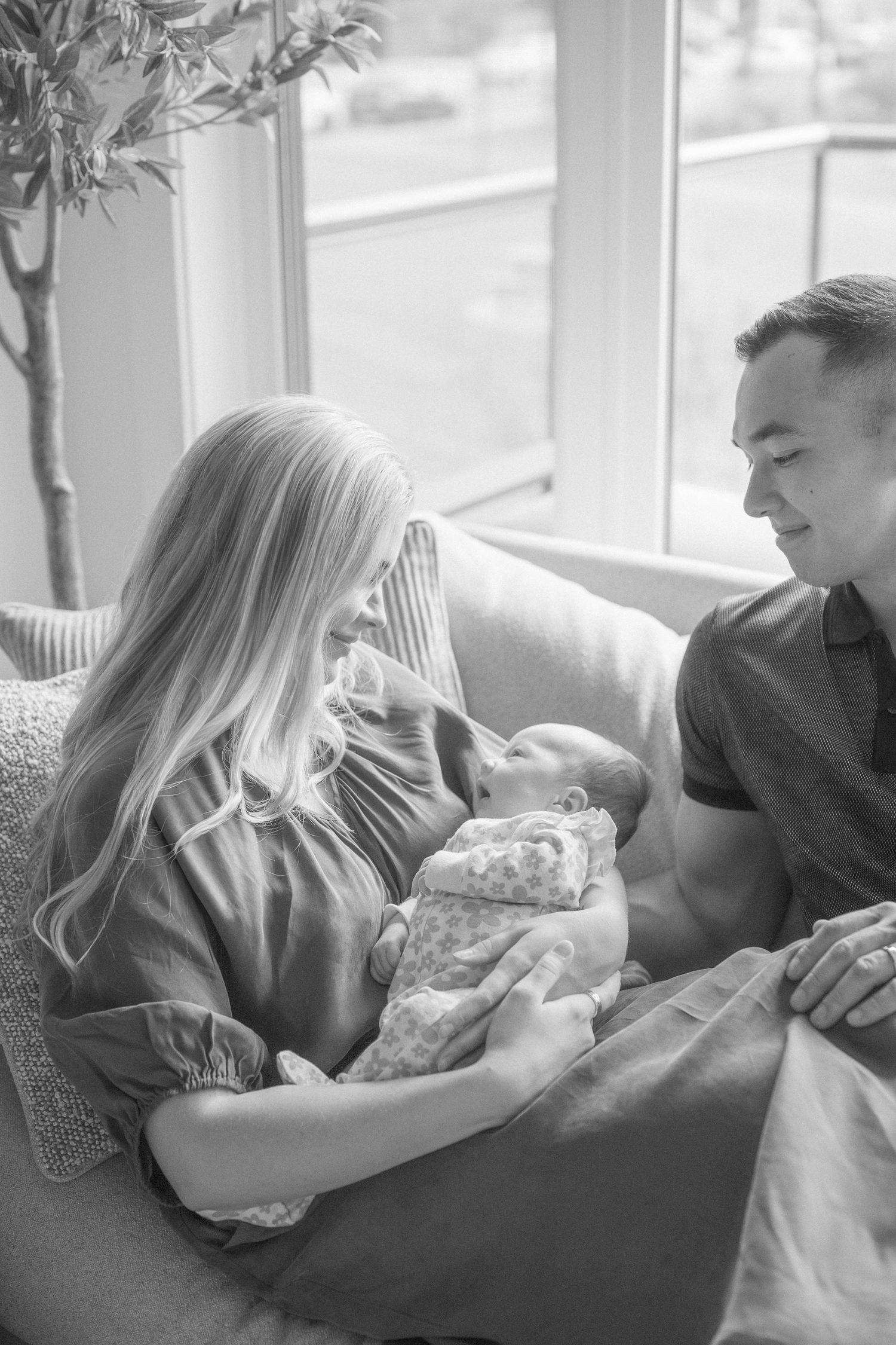 Black and white lifestyle photo showing tender family moments on a couch by bright windows.