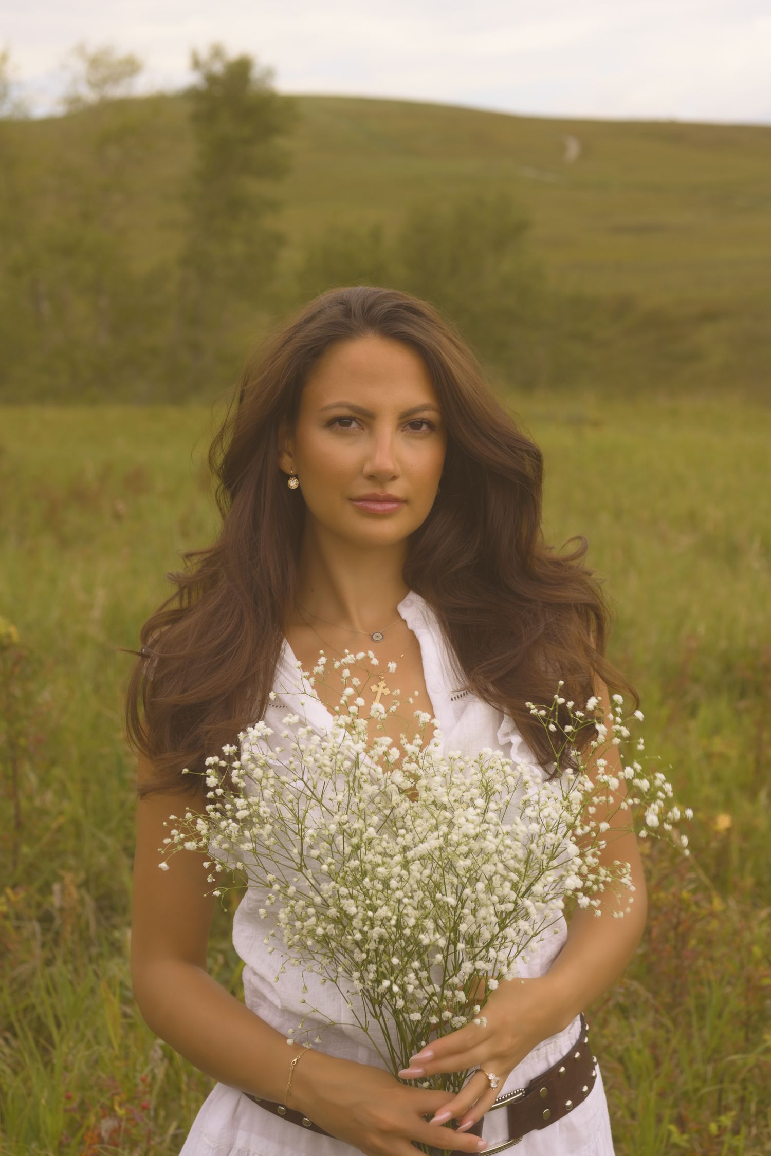 A dreamy portrait in a meadow holding a bouquet of baby's breath flowers against rolling hills.