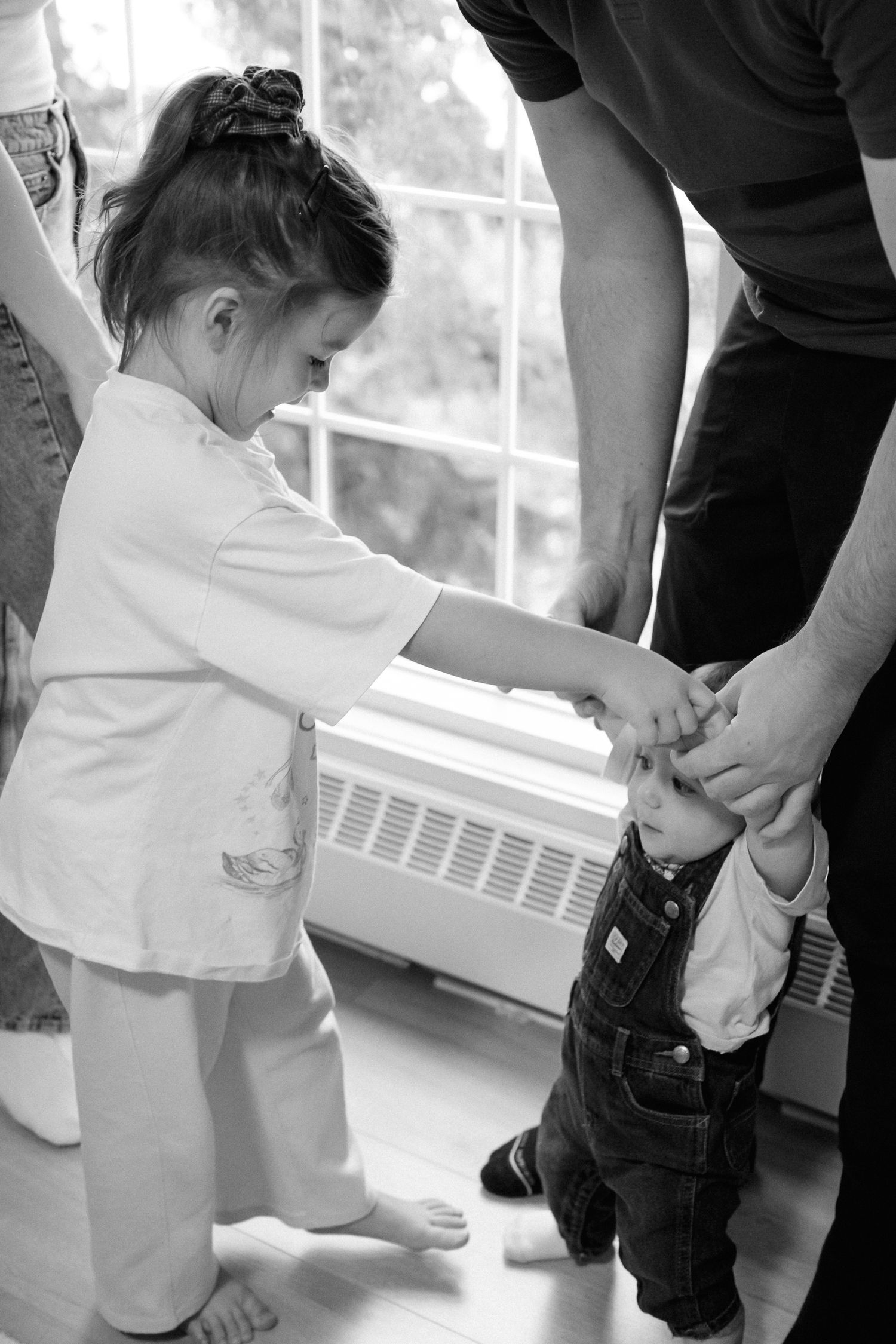 Black and white photo series showing close-up details of a toddler learning to walk with adult support.