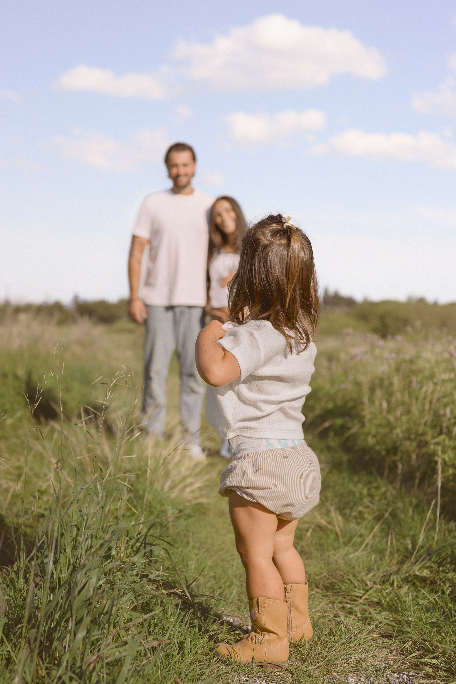 Child running through tall grass towards adults in a sunlit meadow.