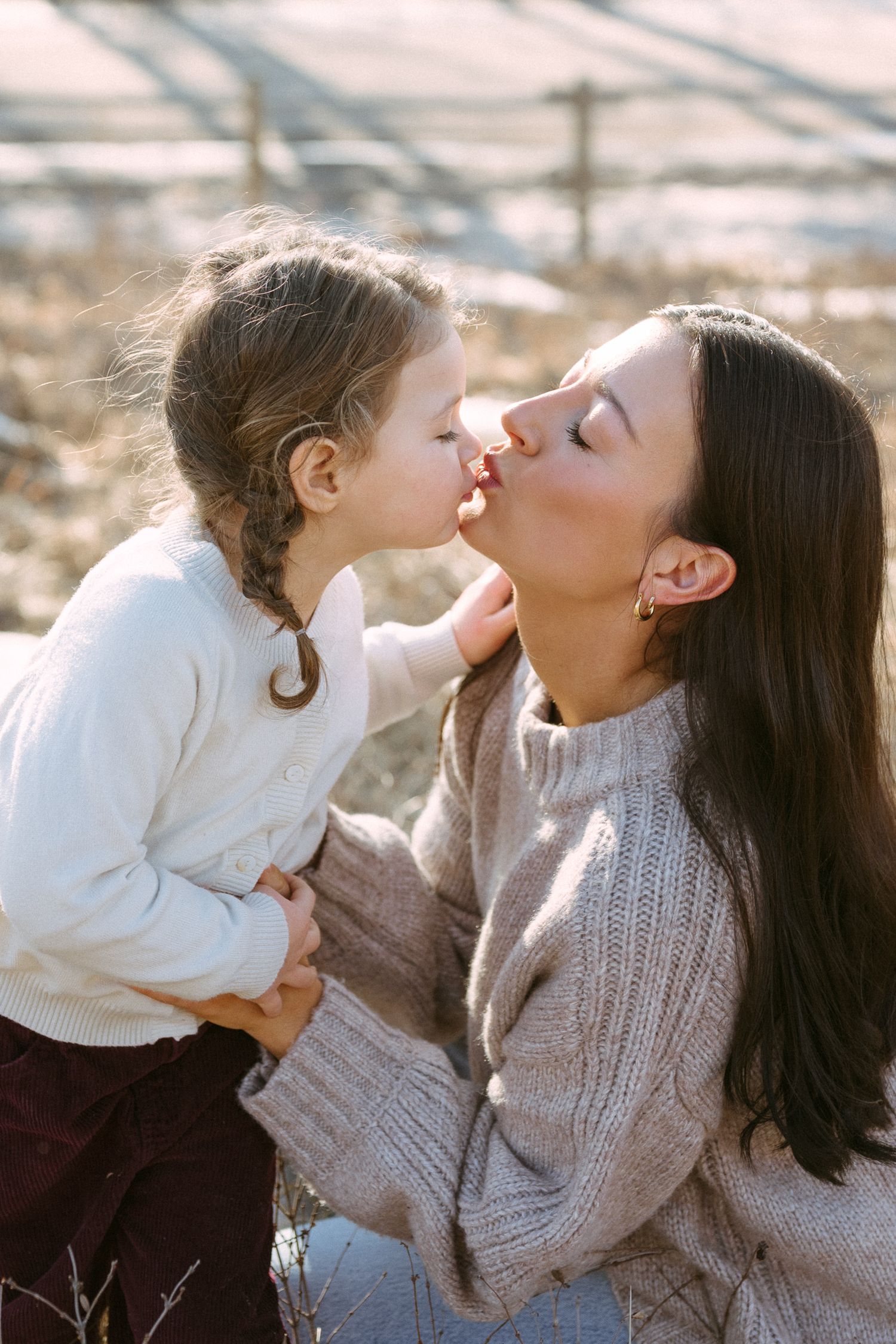 A tender moment shared between parent and child wearing cozy sweaters in natural outdoor lighting.