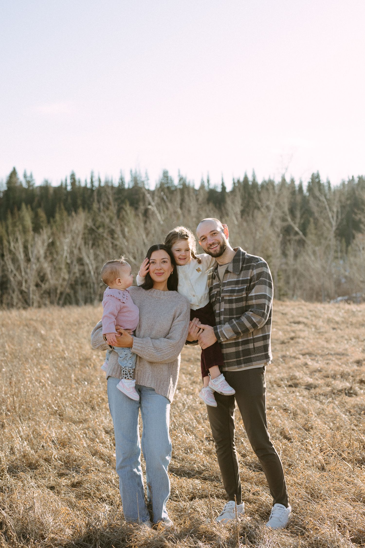 Family spending time together outdoors in a sunny field surrounded by winter trees.