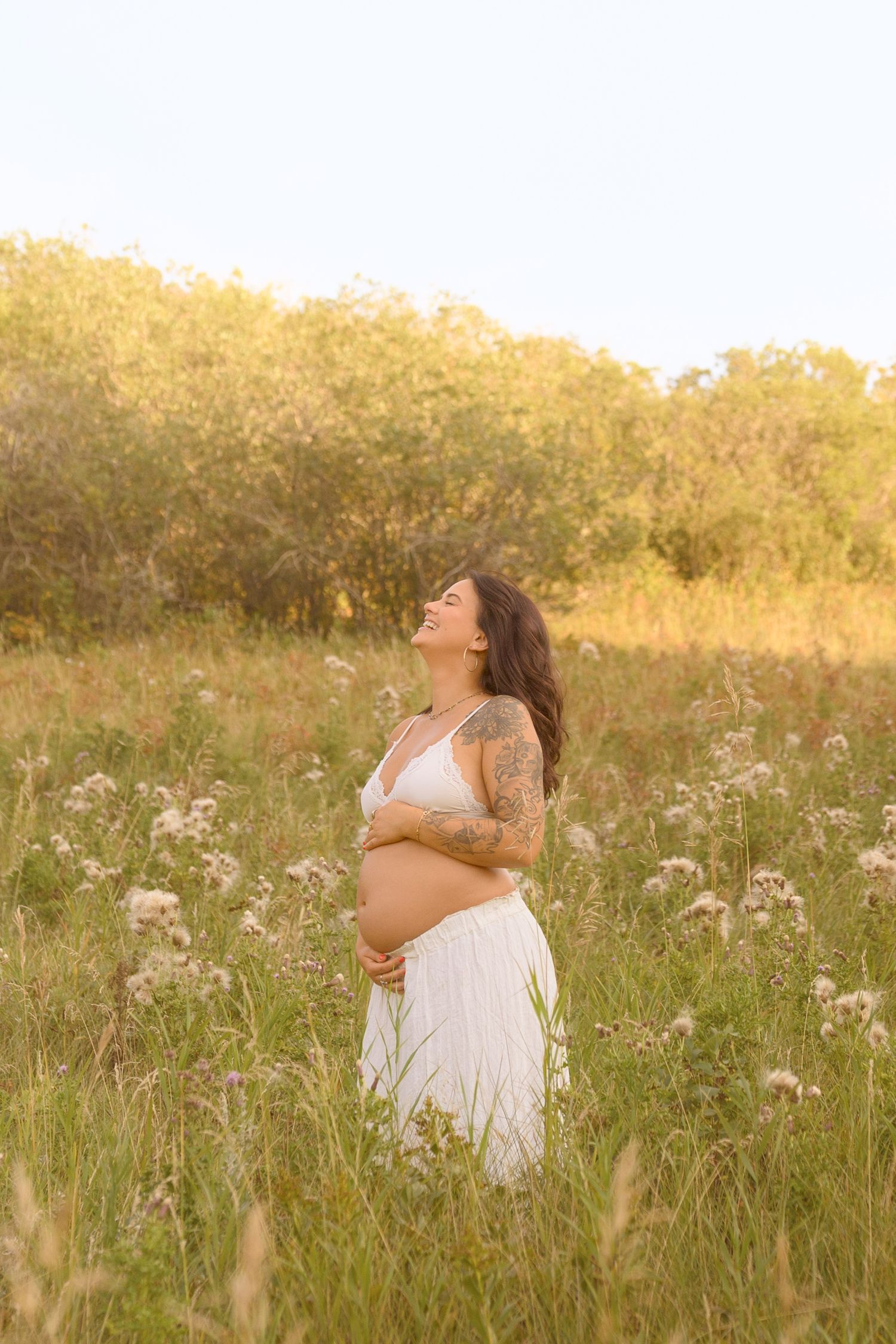A radiant maternity photo session in a meadow with golden light and wild summer flowers.