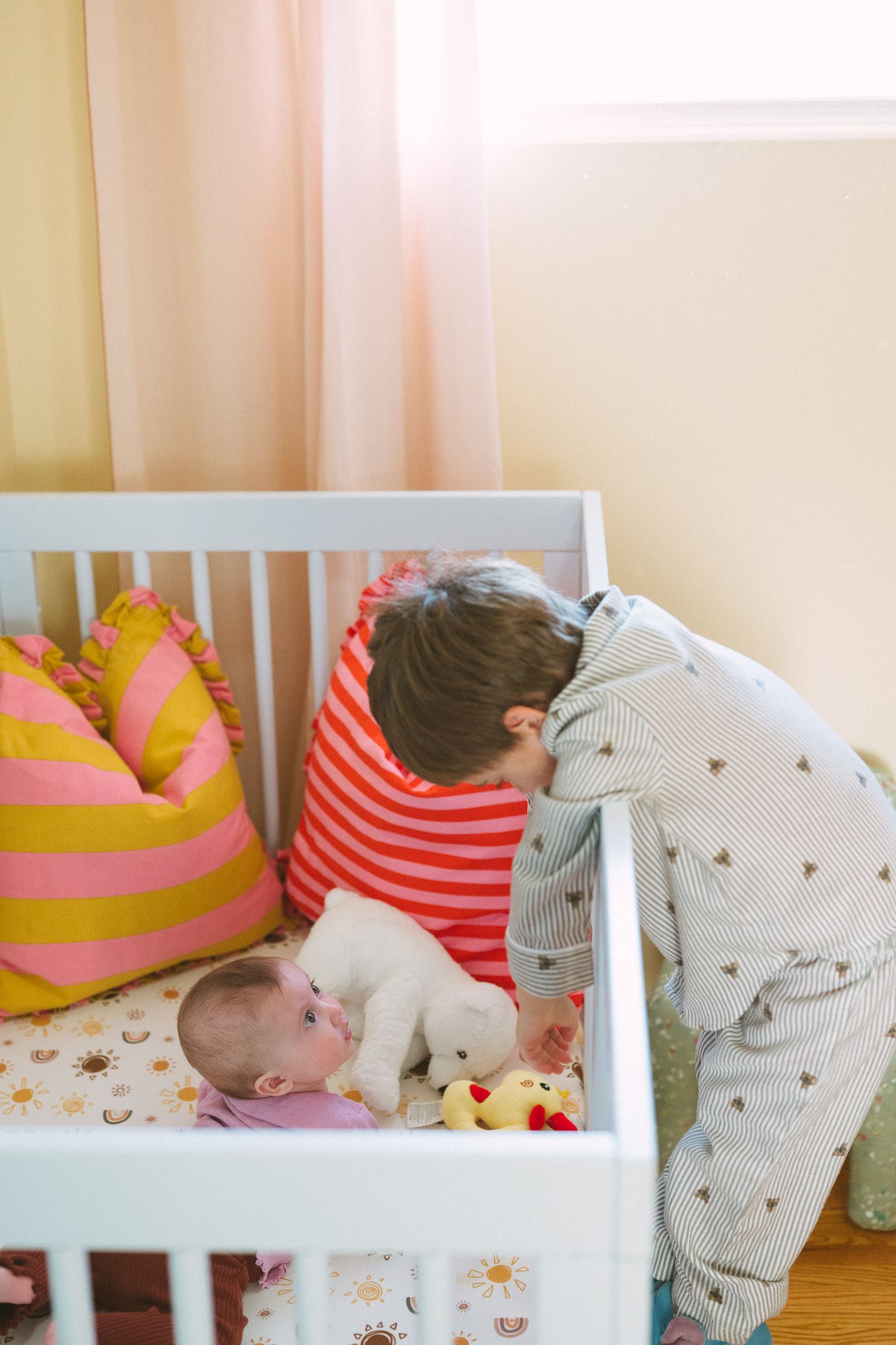 Bright nursery interior with white crib and colorful accent pillows.