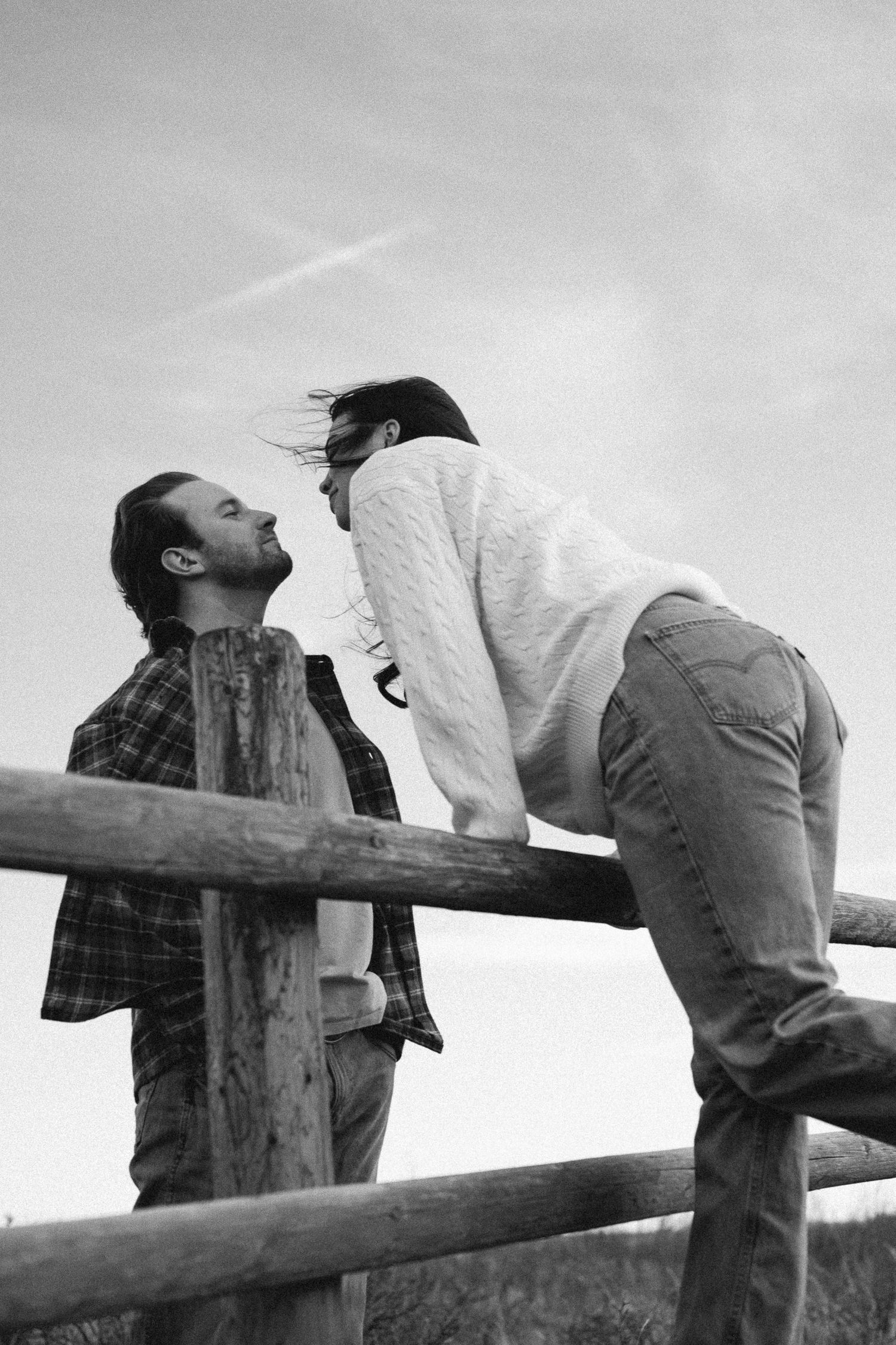 A romantic couple leaning against a wooden fence in black and white sequence.