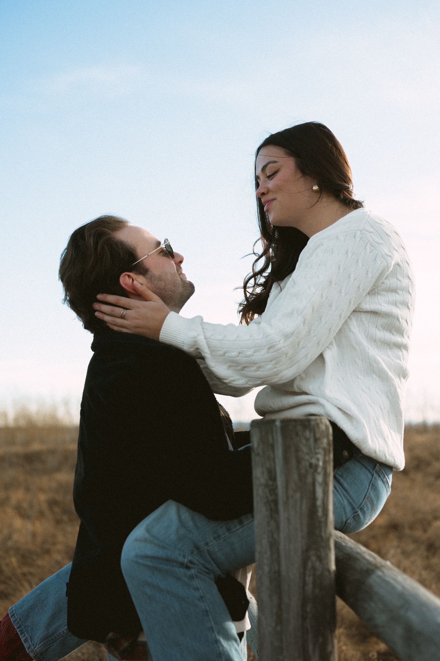 Romantic couple sharing intimate moment by wooden fence in golden afternoon light.