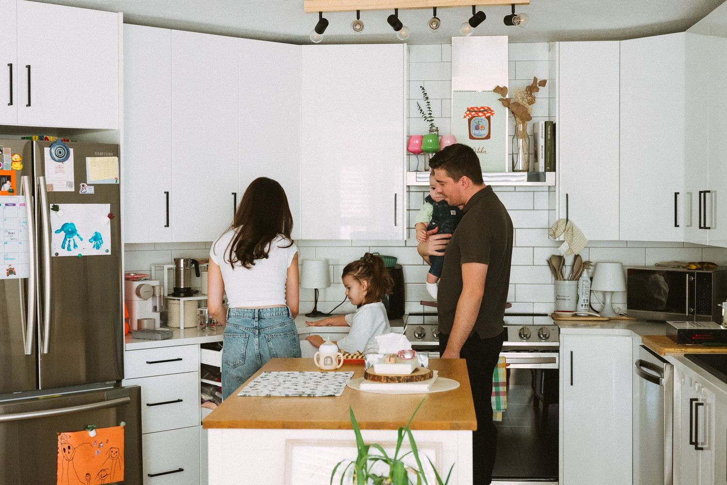 A family spends quality time together in a bright modern kitchen with white cabinets and wooden countertops.