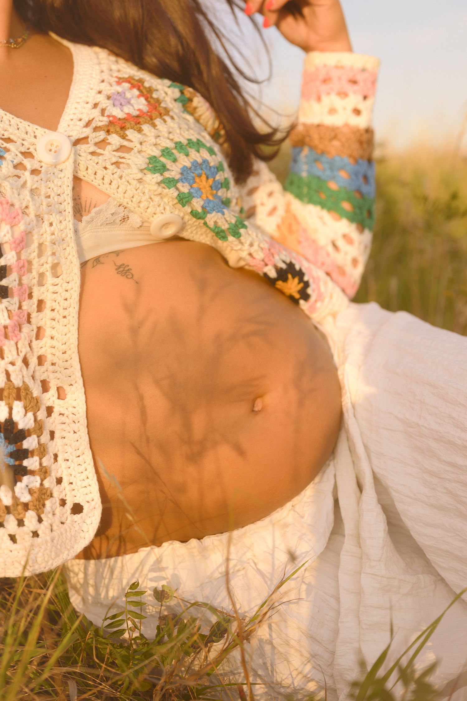 Woman in delicate white lace dress lying in sunlit grass during golden hour photography session.