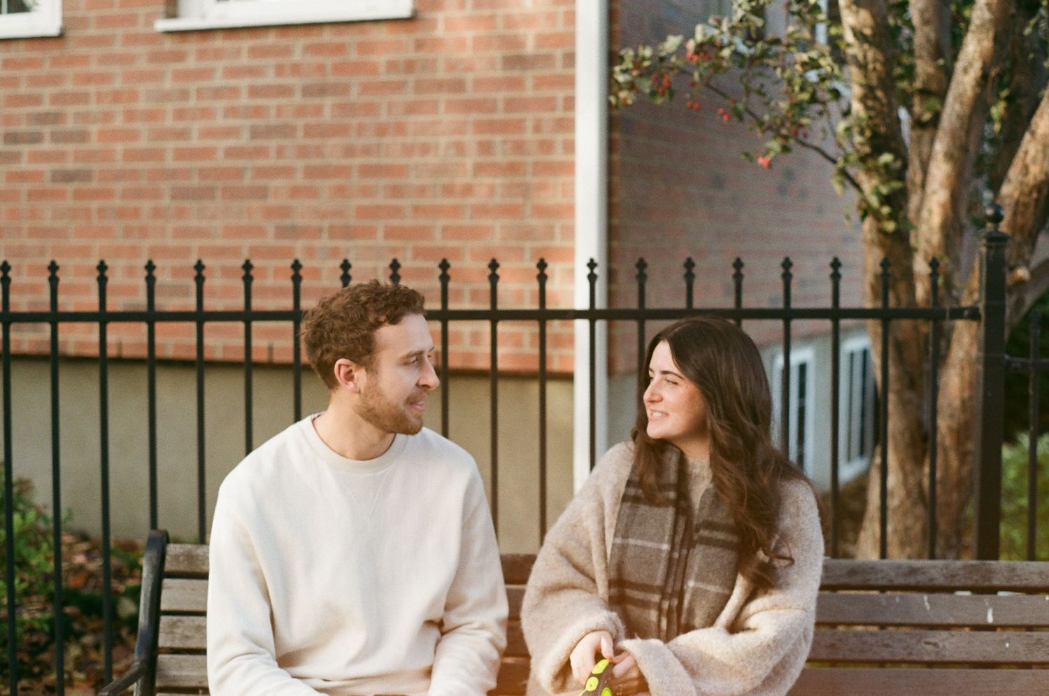 A couple sits on a wooden bench outdoors while enjoying a conversation in a garden setting.