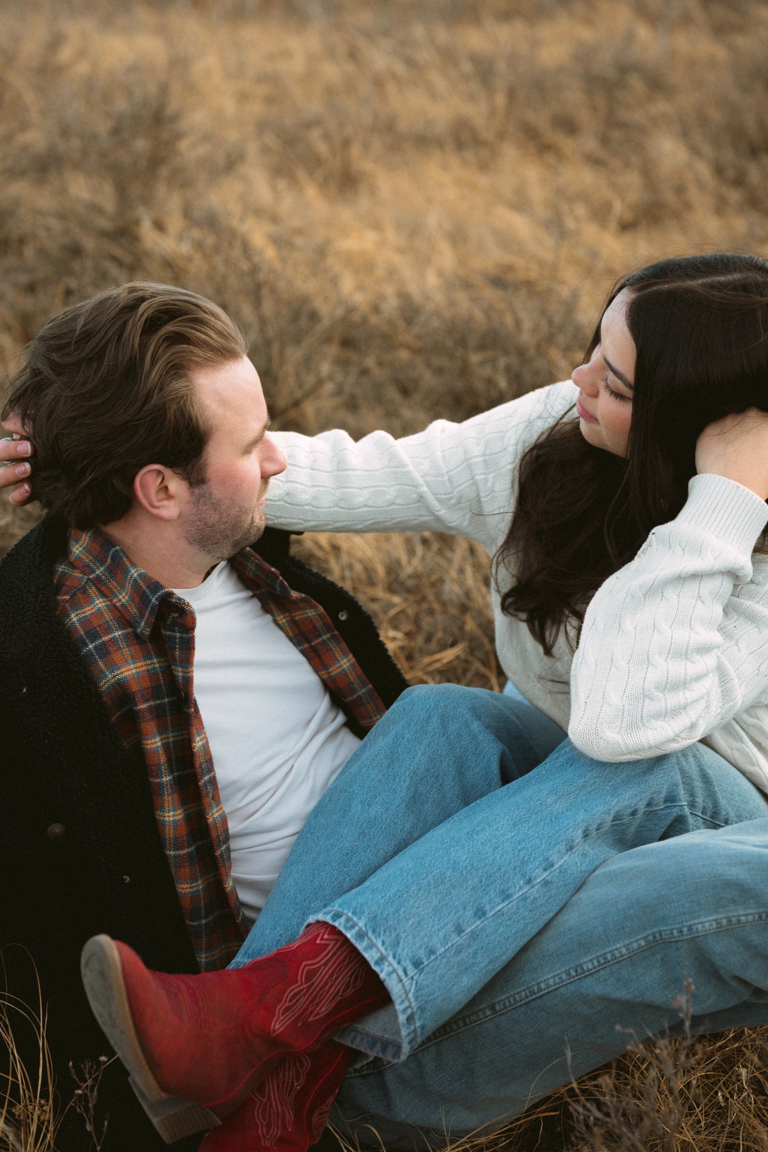 Couple in casual clothing lying together in dry grass field sharing tender moments.