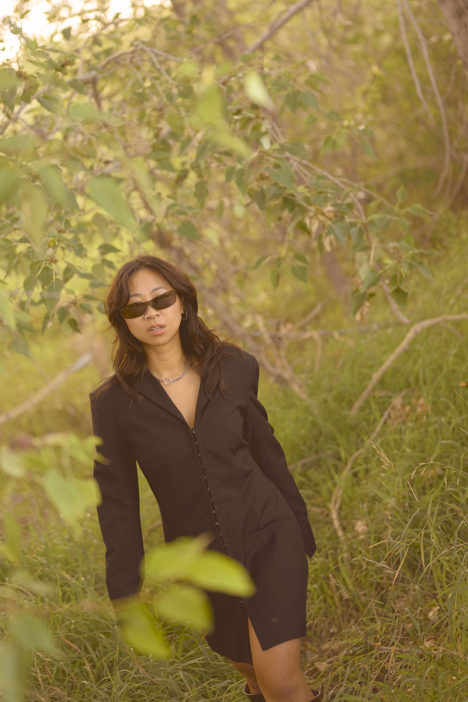 A stylish black dress ensemble captured among leafy branches in natural lighting.