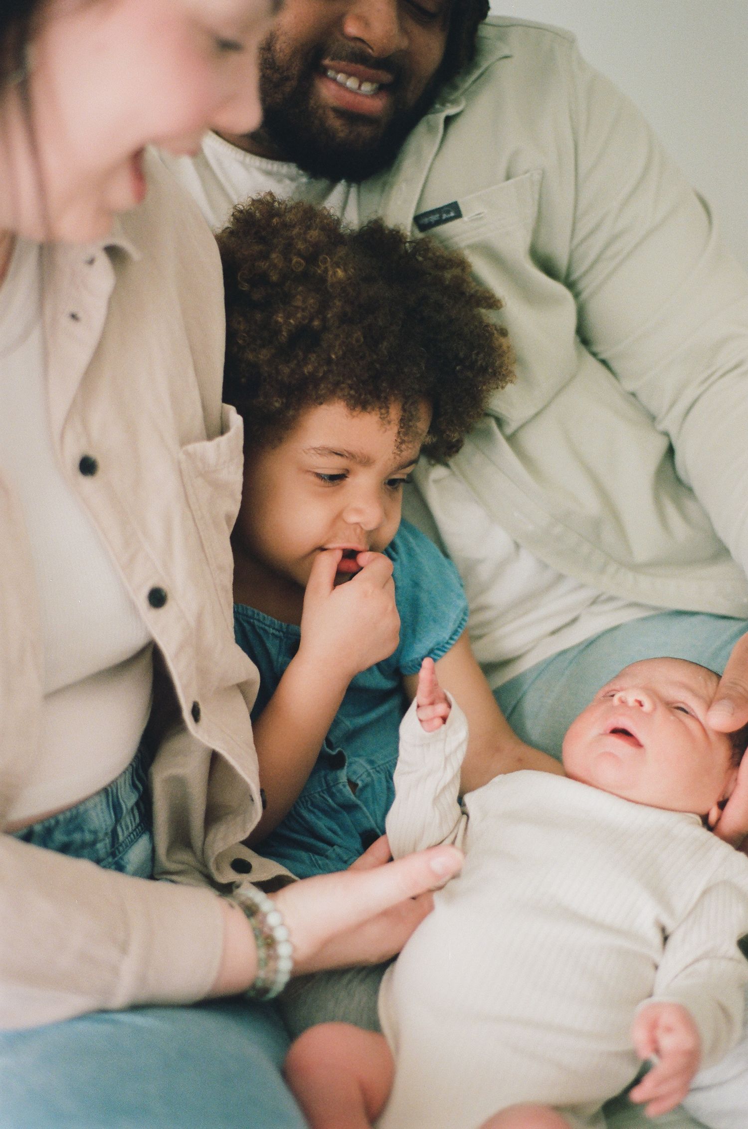 Family of four admiring their newborn baby together, with toddler and parents sharing a tender moment.