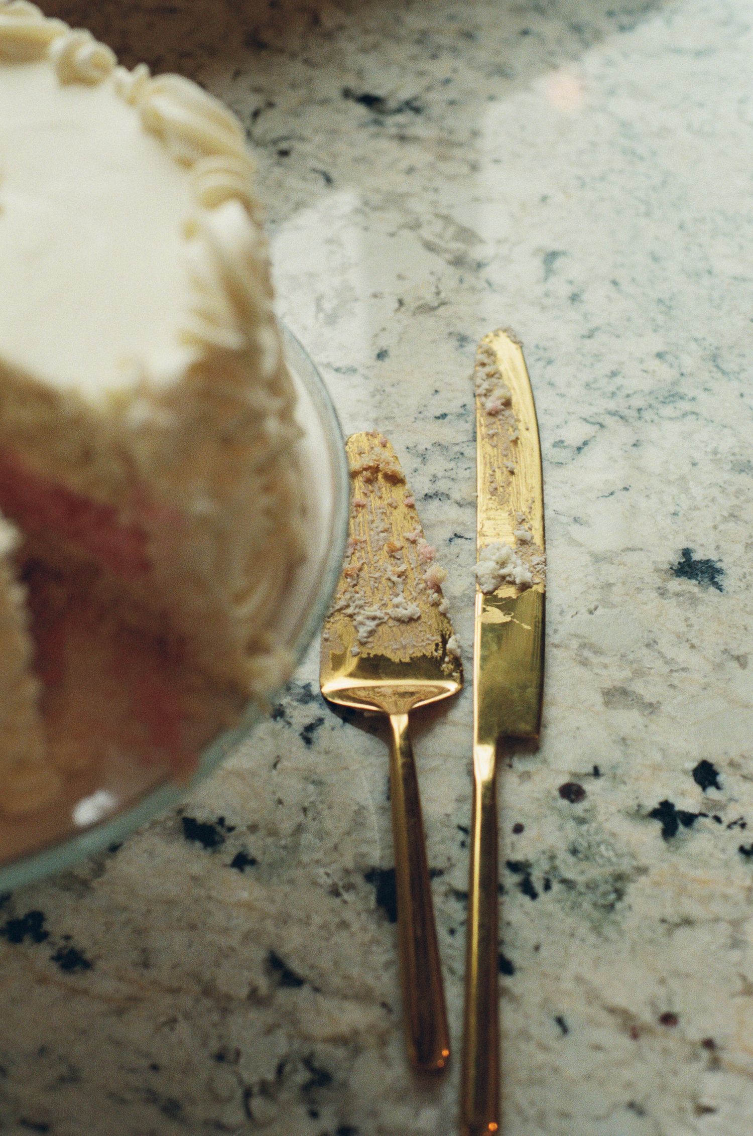 Gold cake server and knife with frosting on marble countertop beside a white frosted layer cake.