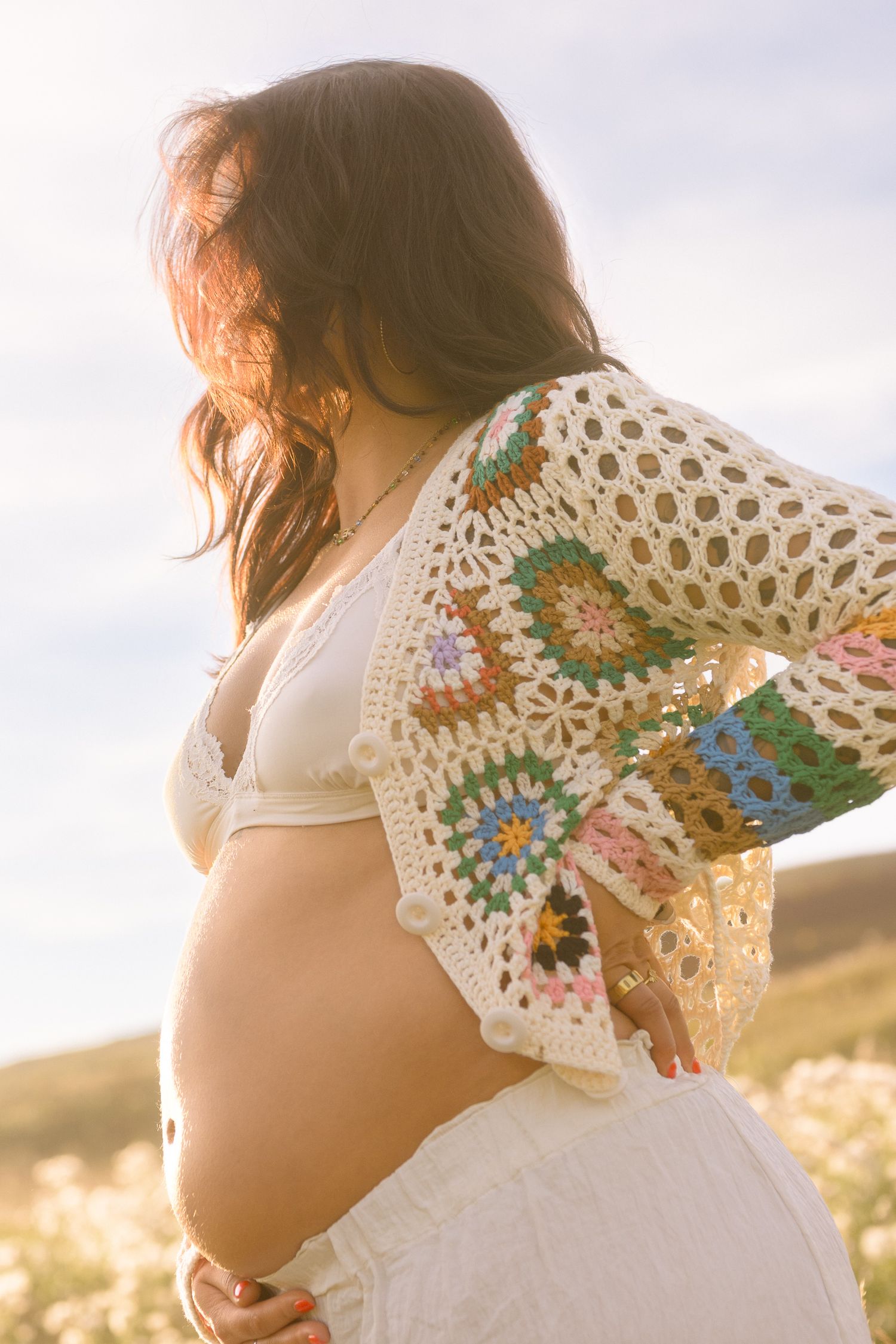 A close-up maternity photo highlighting a handmade crochet cardigan and white lace bralette.