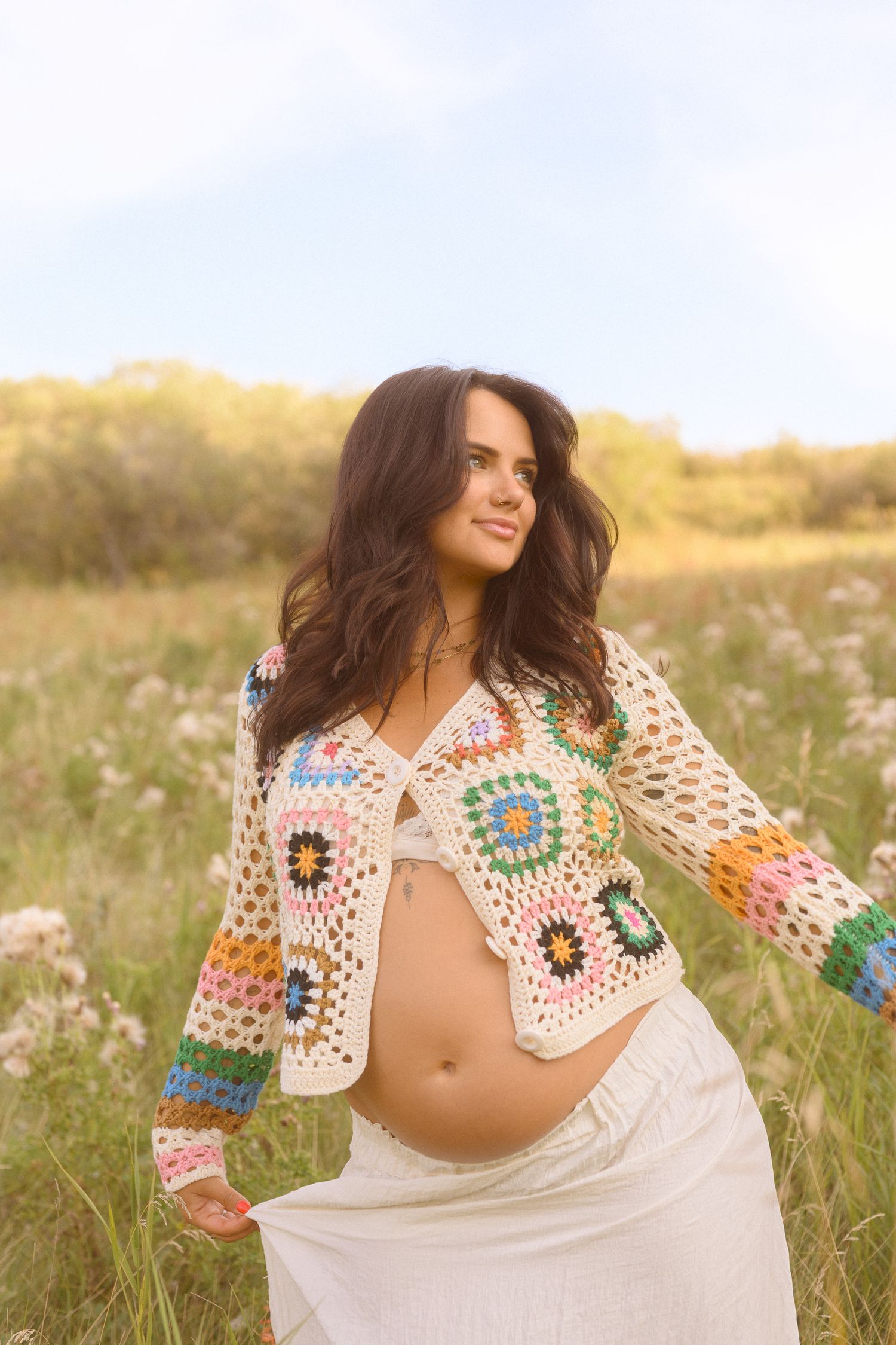 Ethereal maternity portraits showcase a handmade rainbow crochet shawl against tall grass.