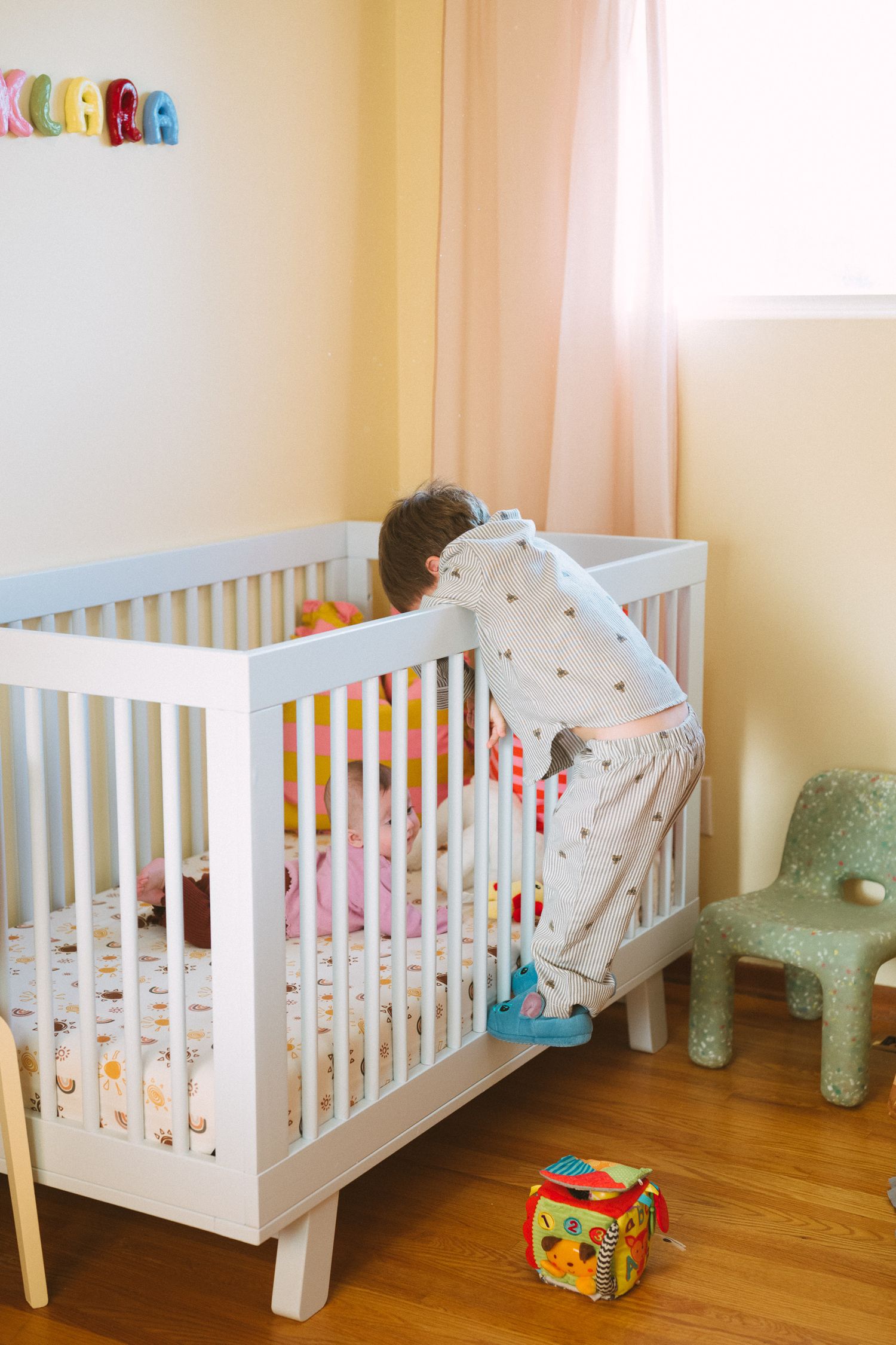 White crib in corner of nursery with colorful toys and mint green accents.