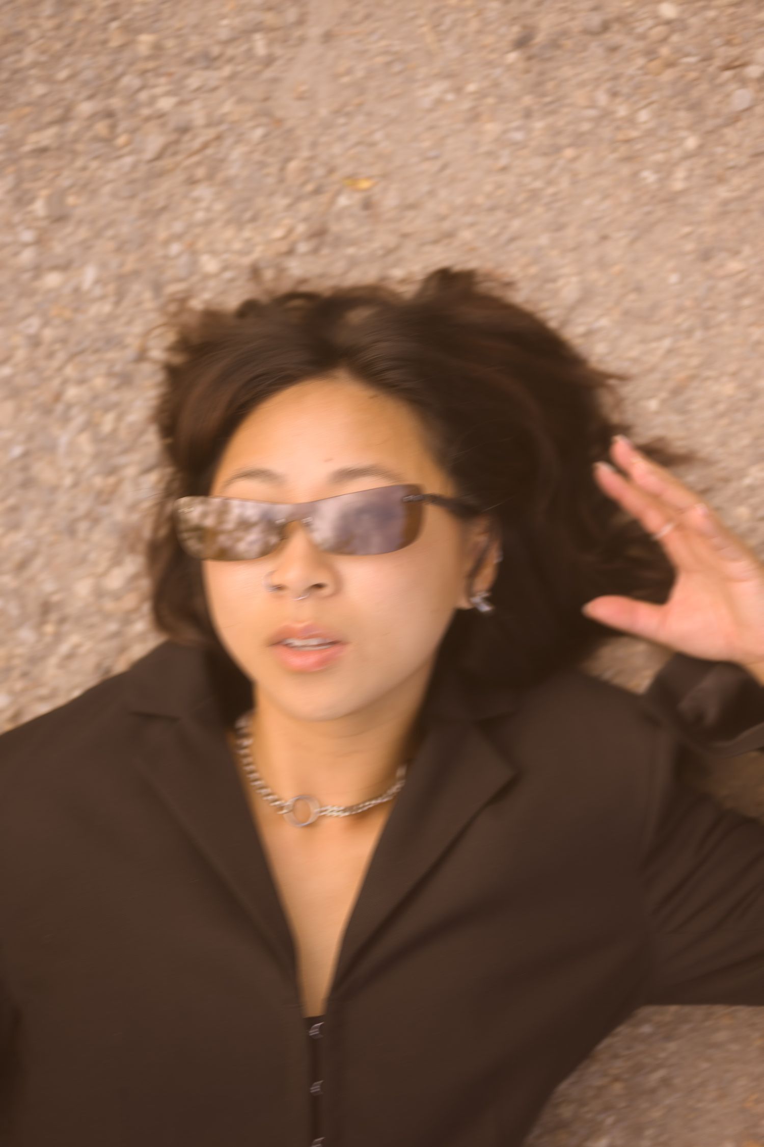 Close-up portrait of someone in sunglasses and black blazer lying on concrete.
