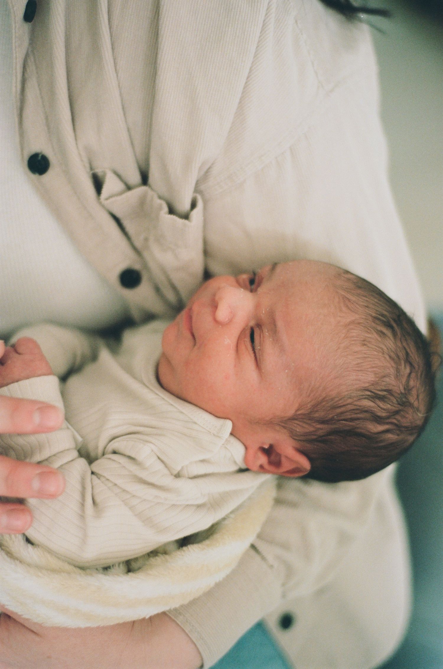 Newborn baby sleeping peacefully in parent's arms wearing a cream onesie.