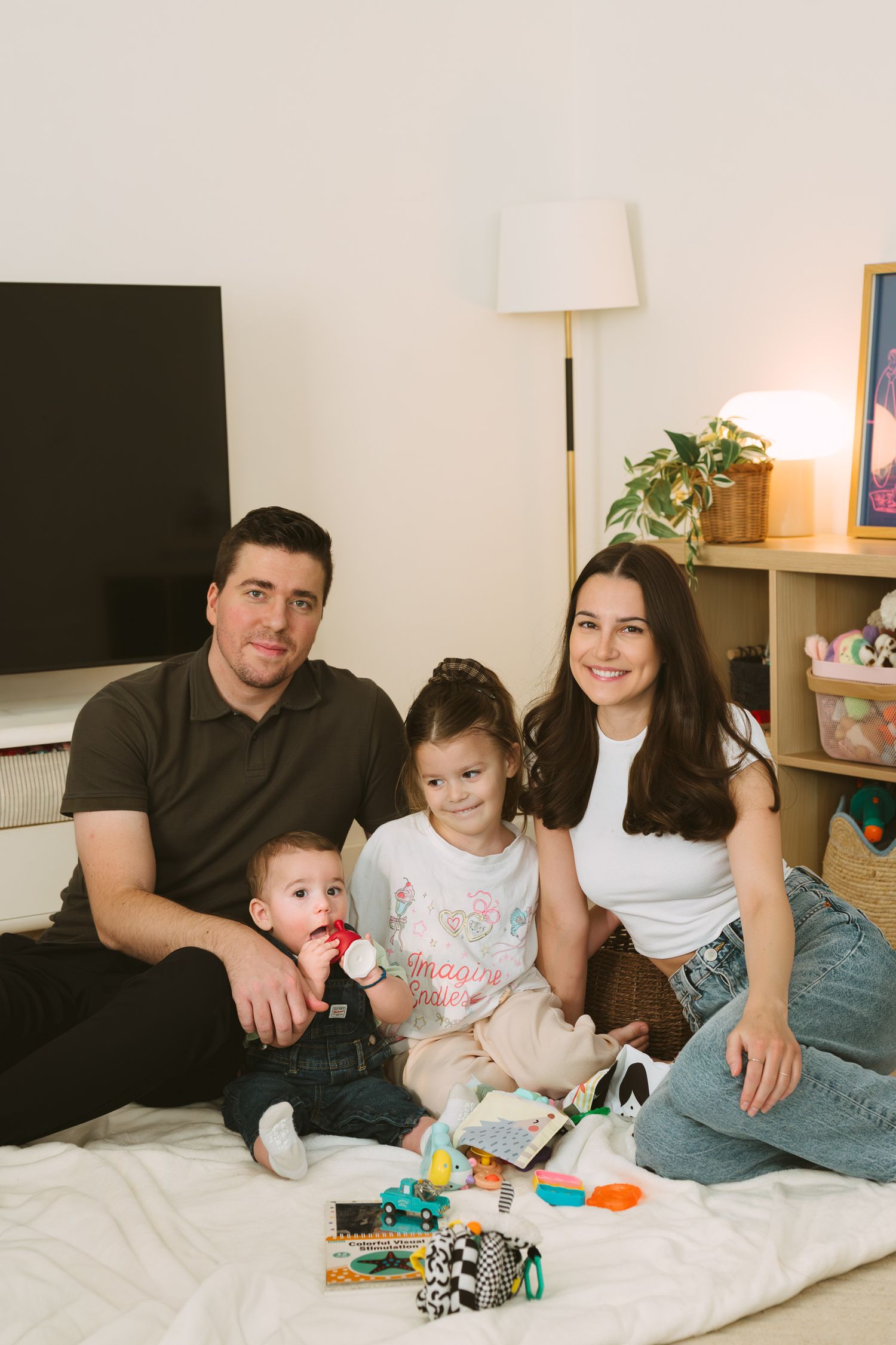 Parents and children relaxing together on white bedding with colorful toys.