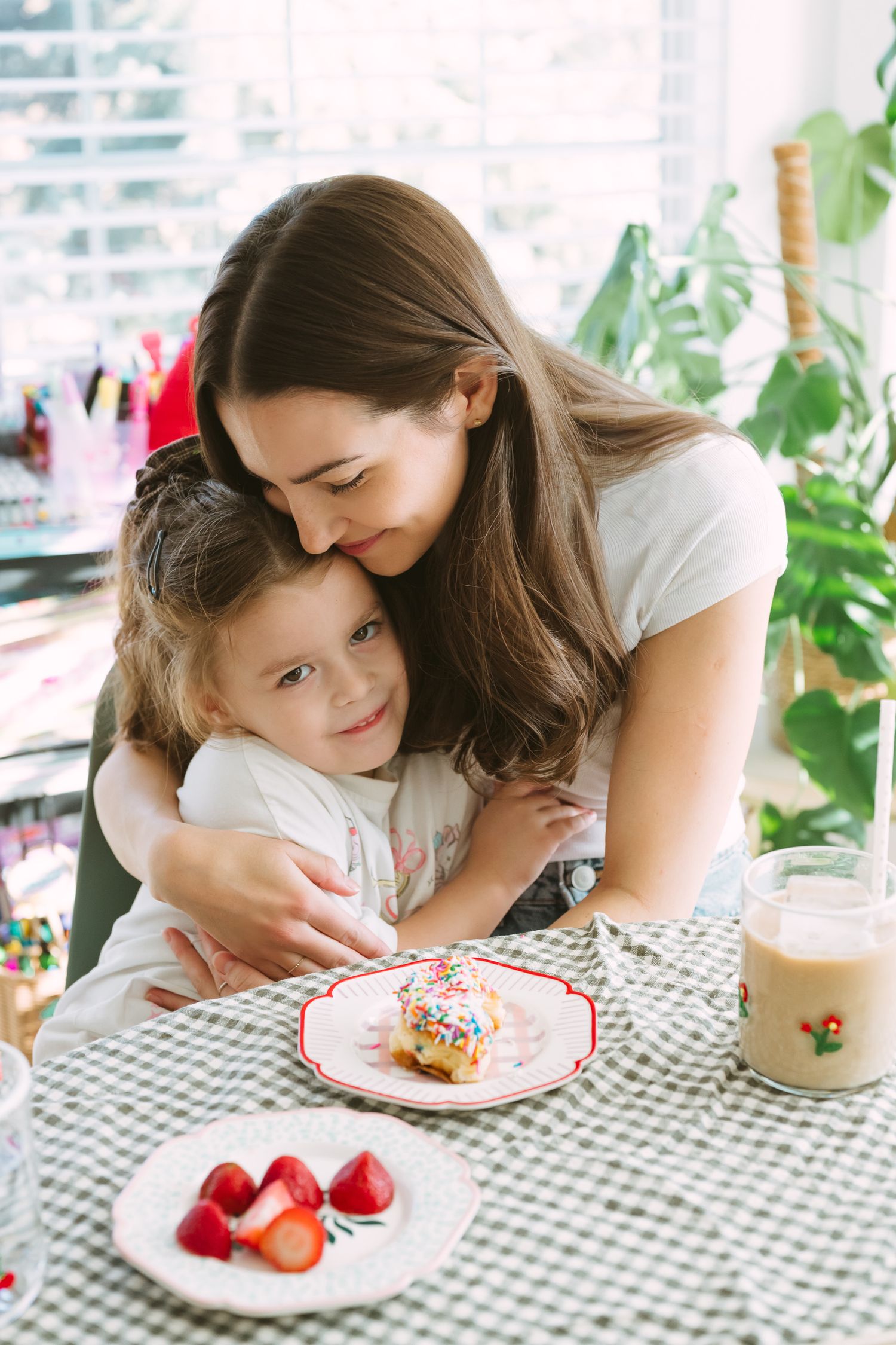 A tender moment shared over dessert and fresh strawberries at a table with a checkered tablecloth by a window.